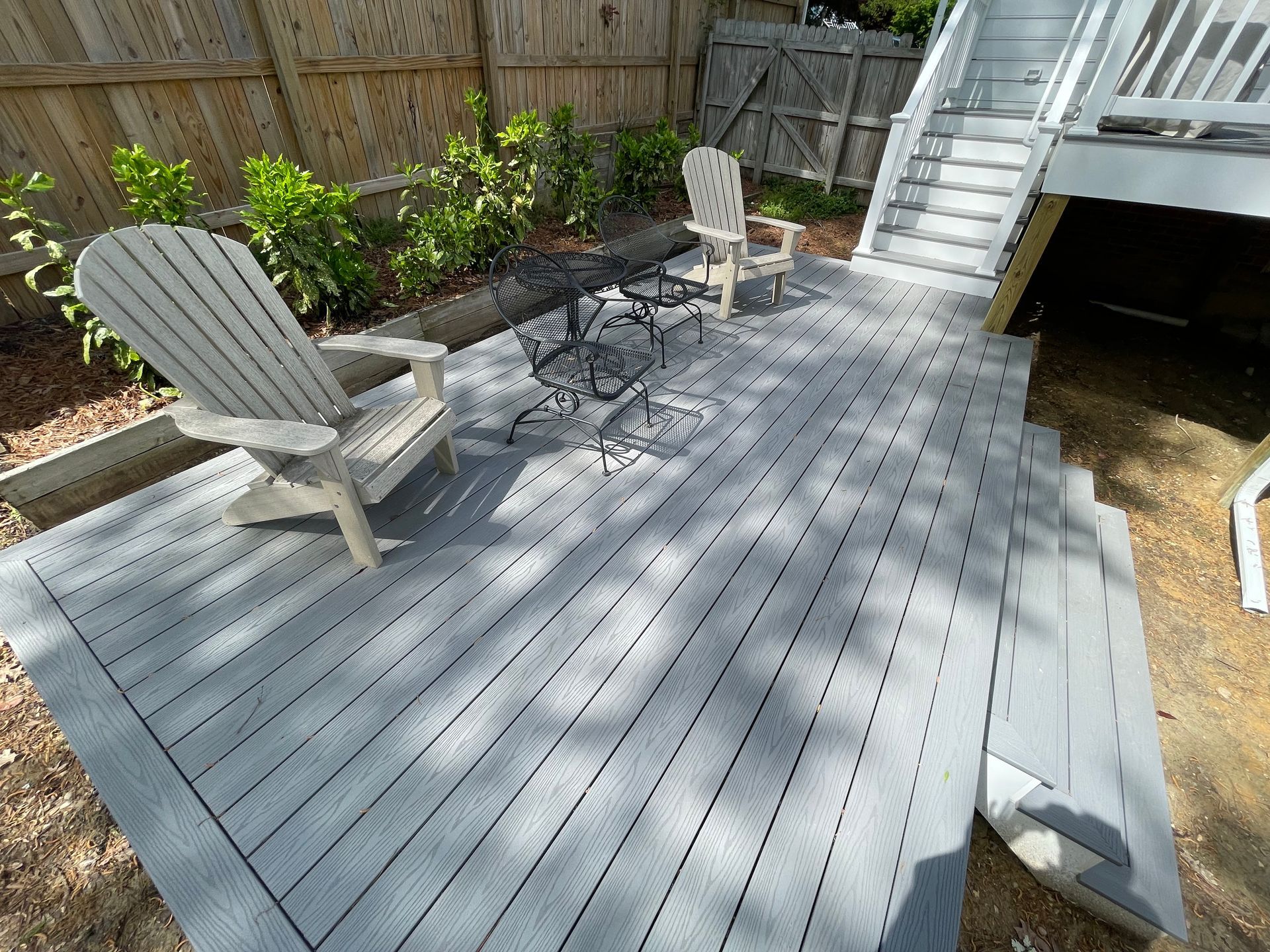 A gray wooden deck with two chairs, a small table, and stairs leading up.