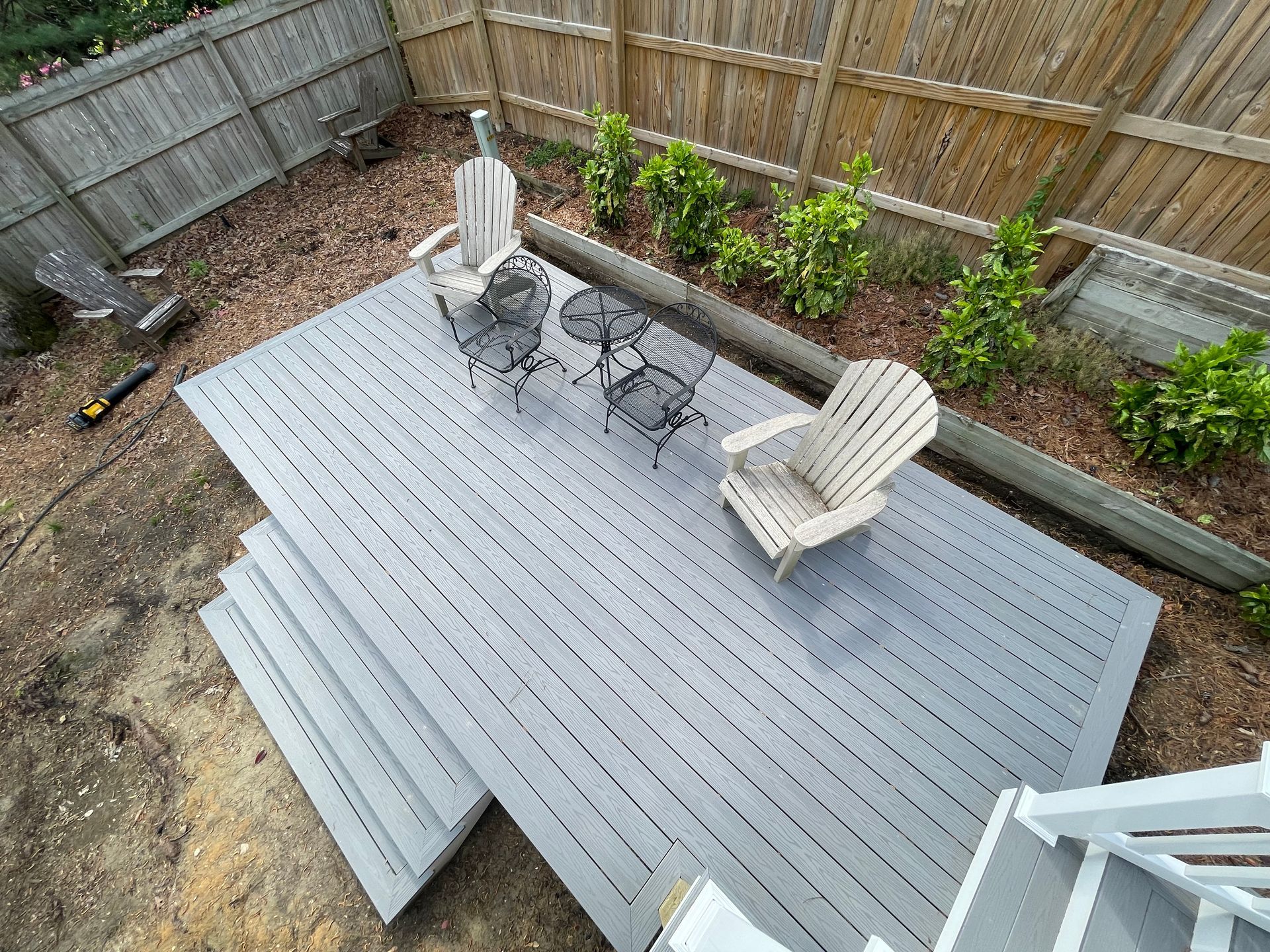 Gray wooden deck with two chairs and a small table in a backyard setting.