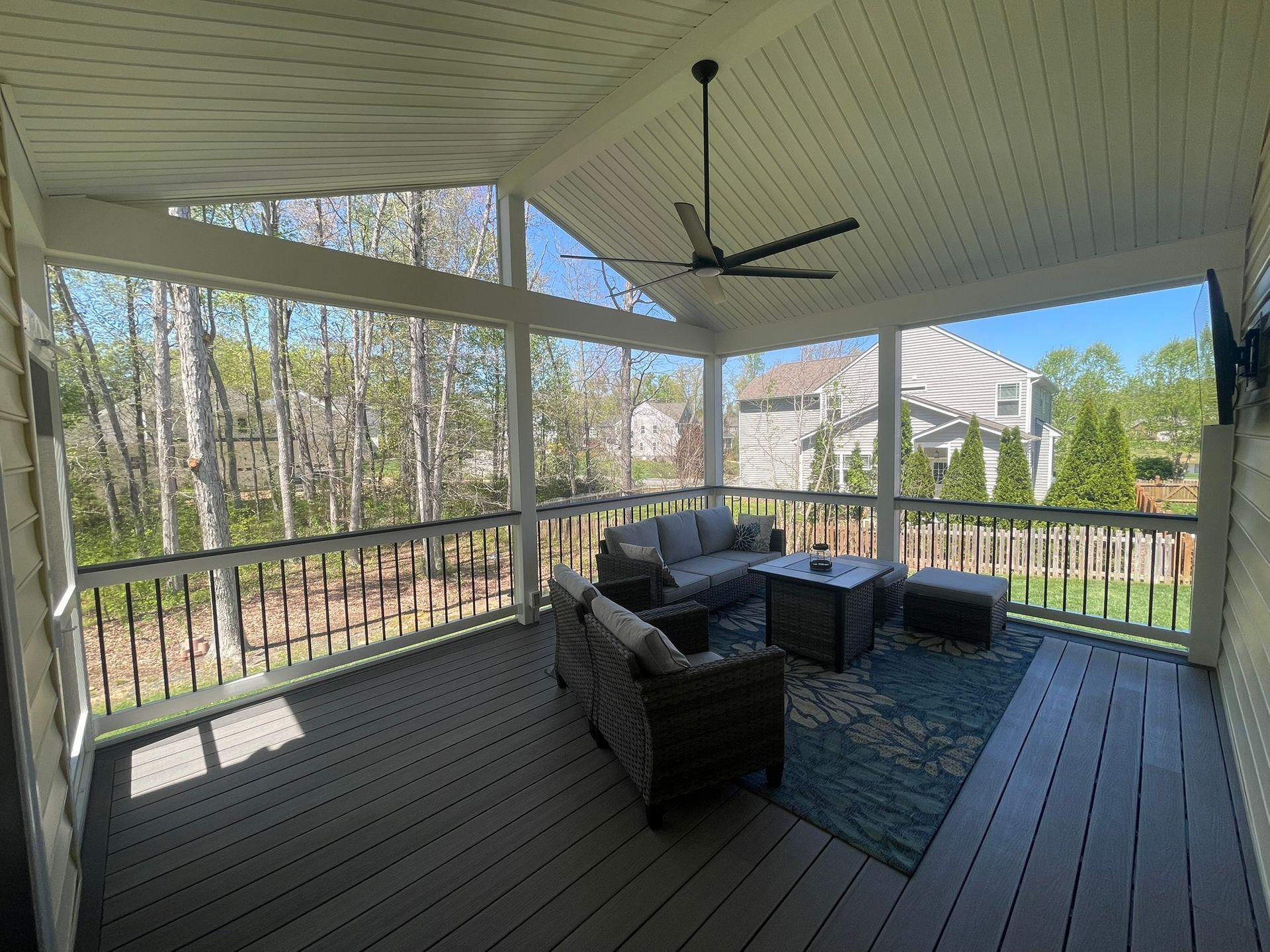 Screened-in porch with outdoor furniture, ceiling fan, and view of trees and homes beyond.