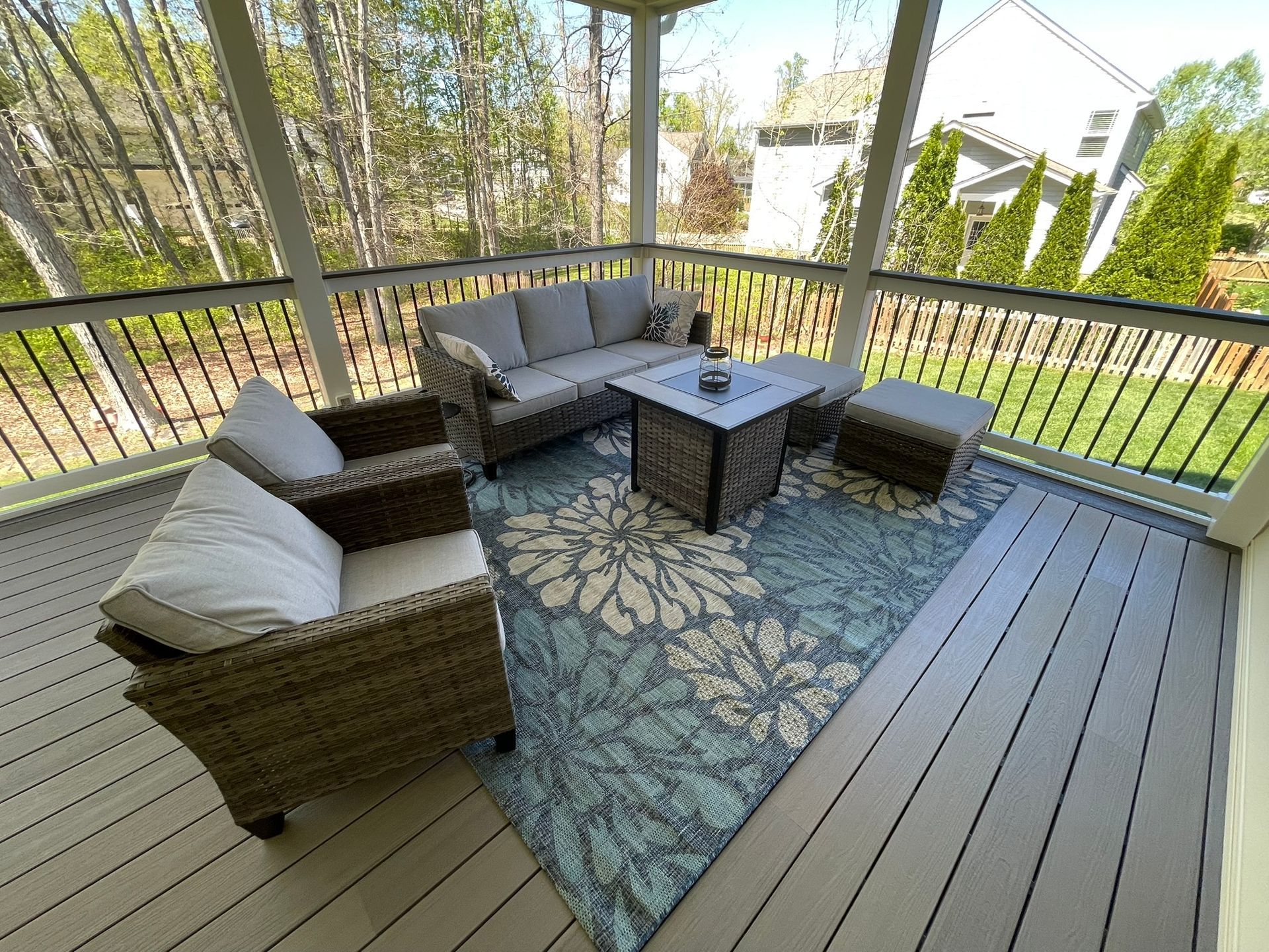 Screened porch with gray furniture, floral rug, and outdoor view.