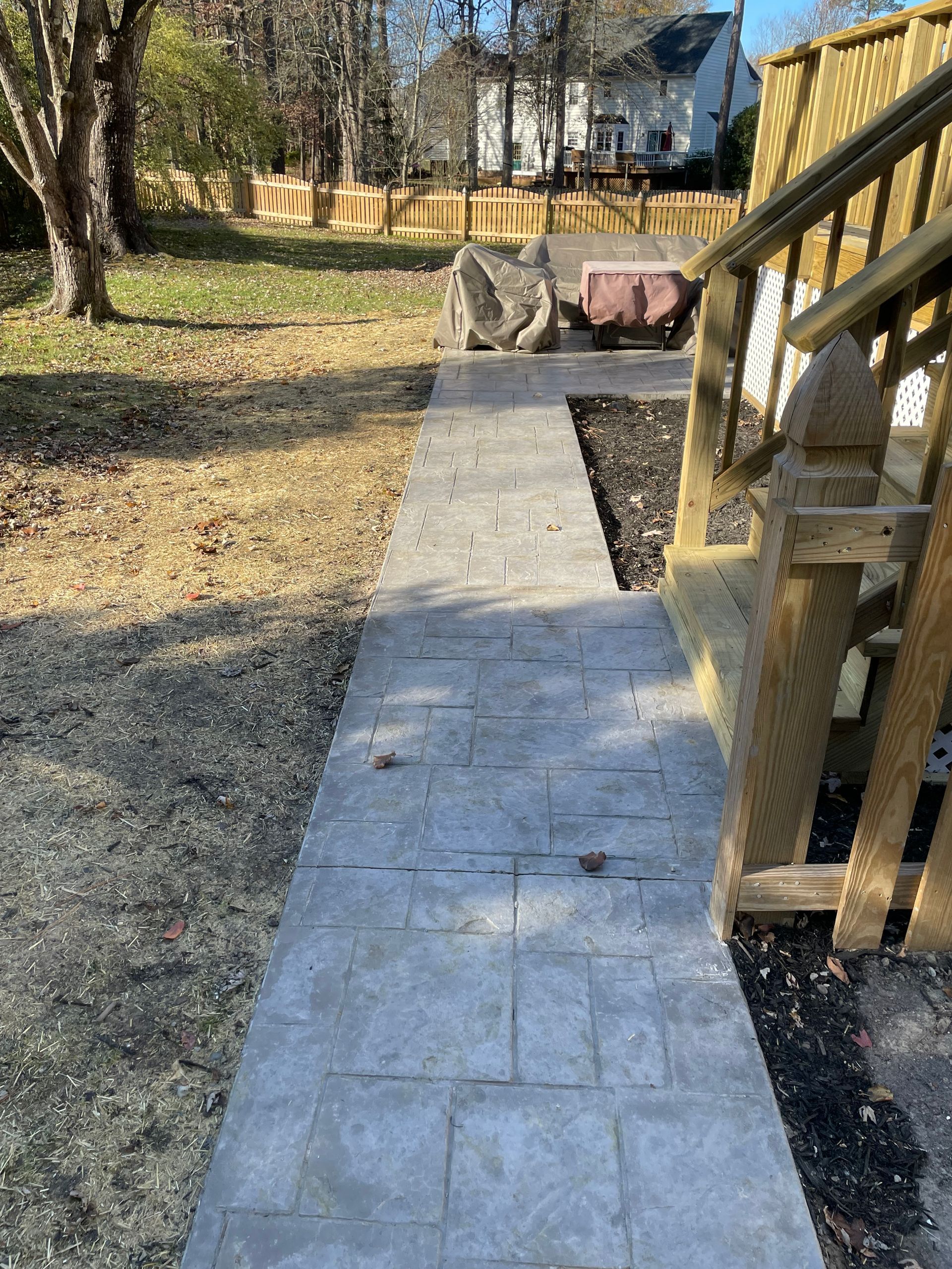 A concrete walkway leading to a wooden deck in a backyard.