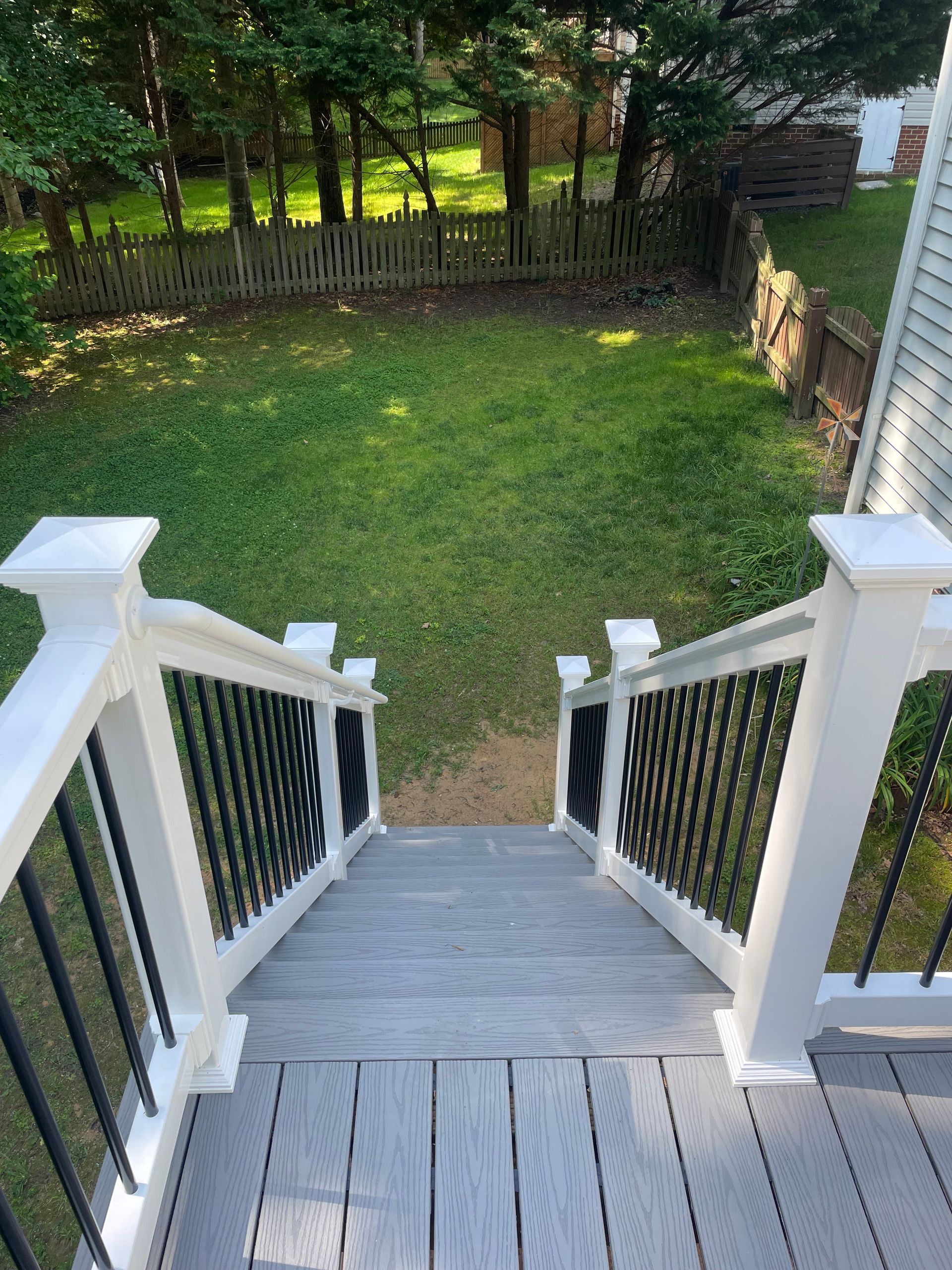 View from deck stairs onto a grassy yard with a wooden fence and trees in the background.