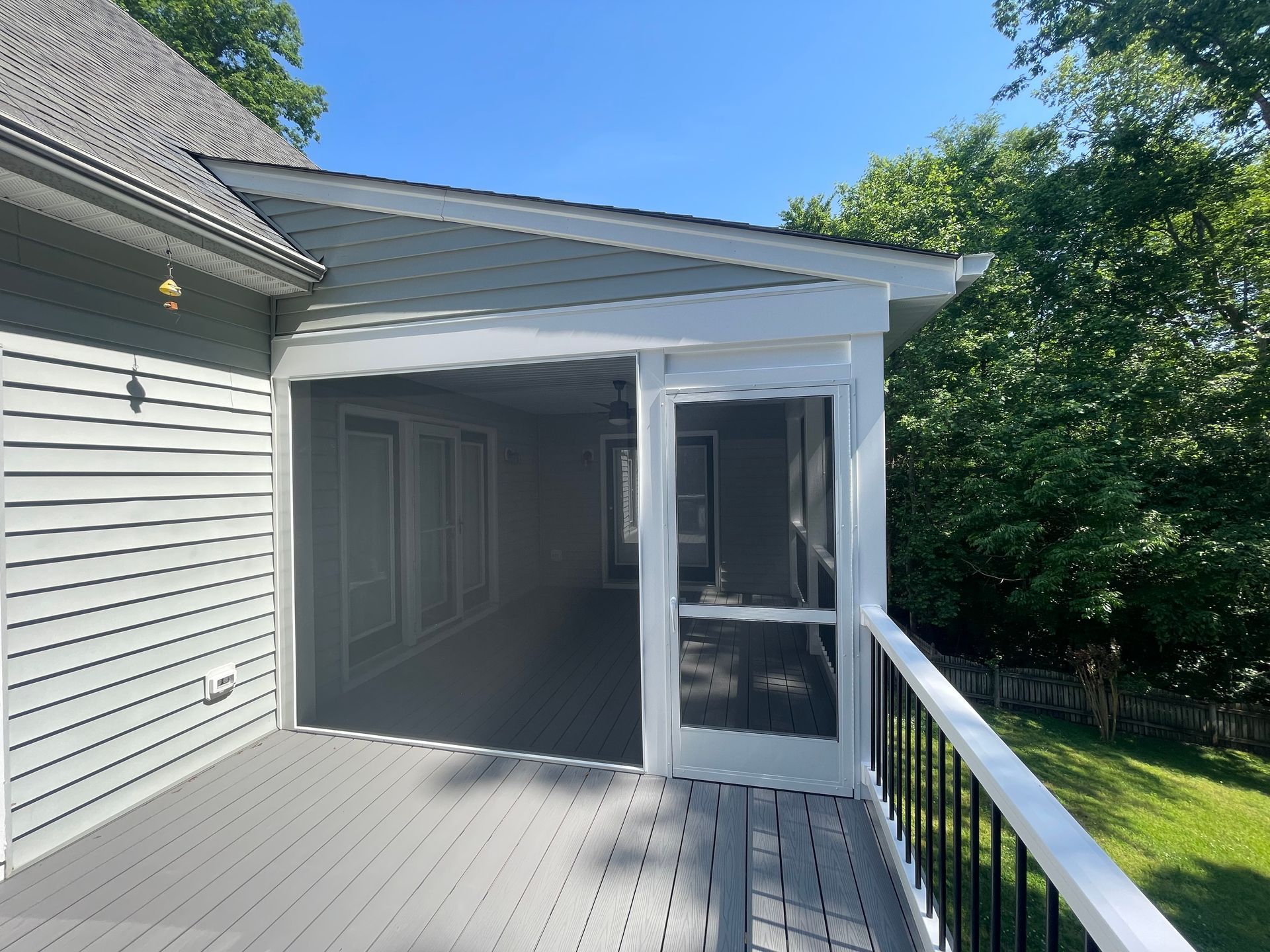 Screened-in porch with gray deck and white trim, overlooking a grassy yard.