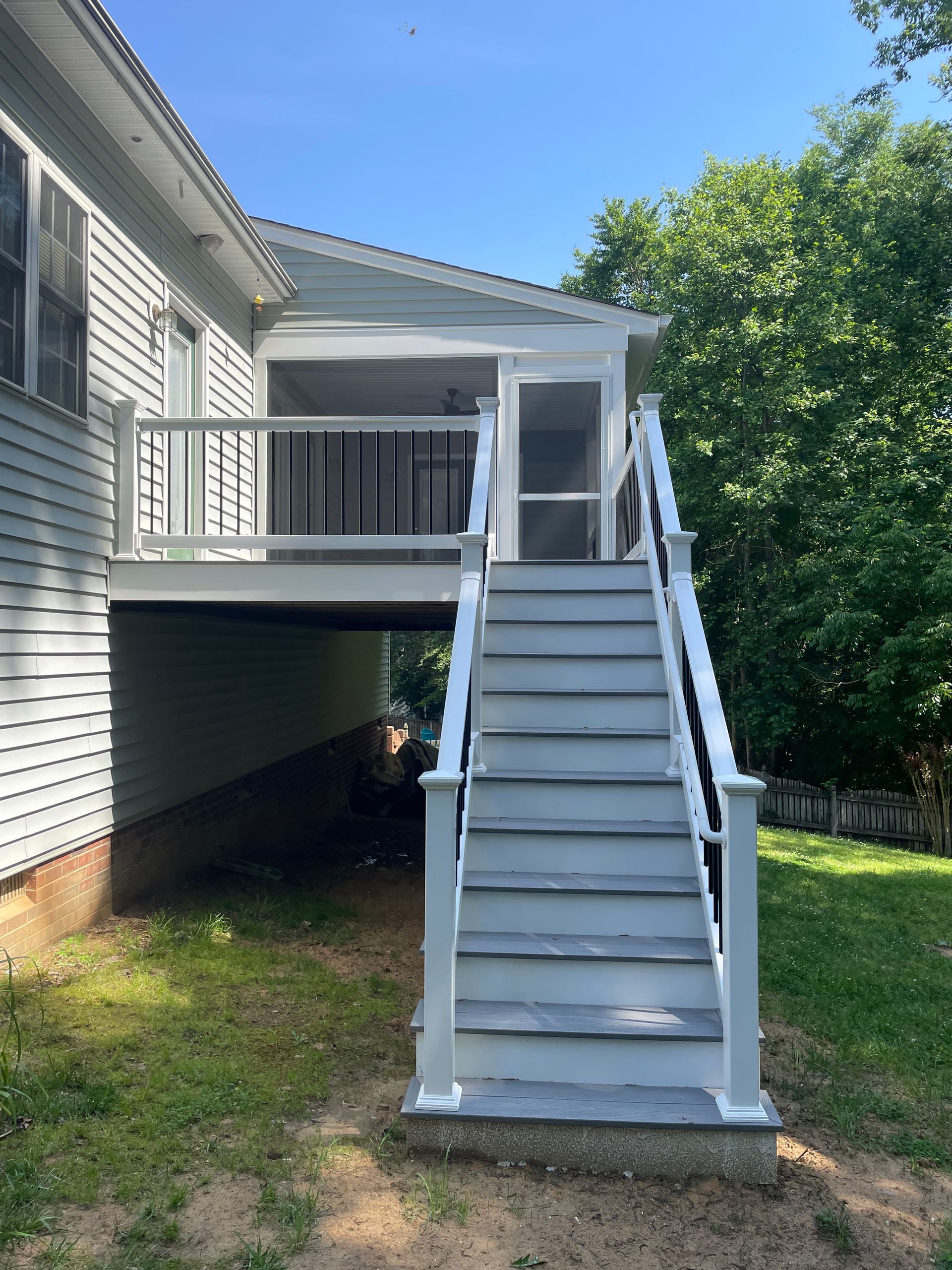 White deck and stairs leading up to a screened-in porch attached to a light gray house.