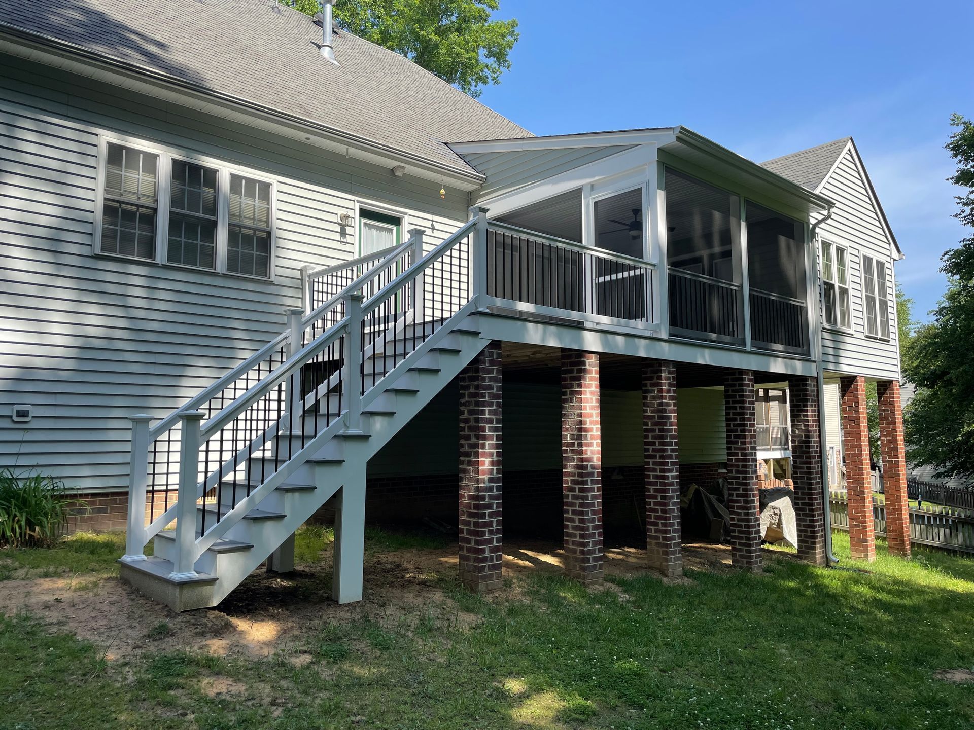 Back of a light blue house with a raised deck and screened-in porch, supported by brick columns; stairway leads down to the yard.