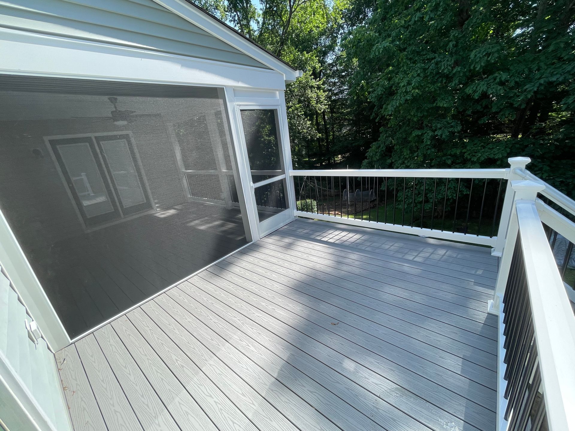 Screened-in porch and deck with gray composite decking and white railing, black metal balusters. Forest backdrop.