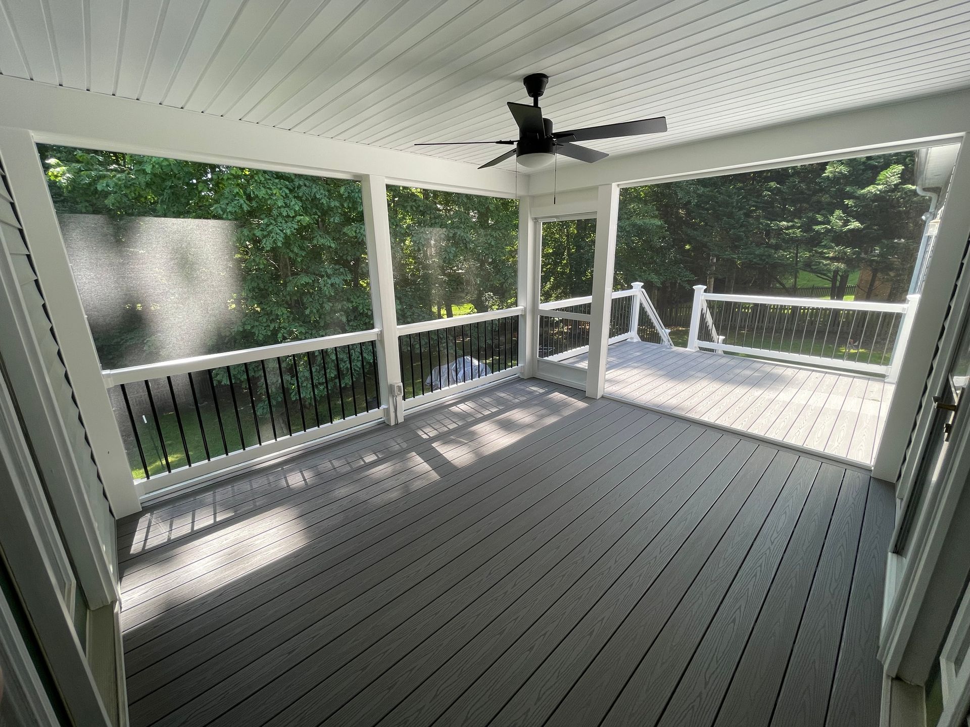 Screened porch with gray flooring, white trim, and a ceiling fan; views of trees.