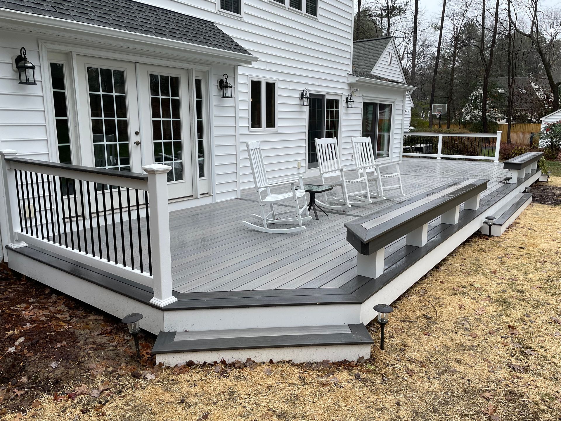 There is a large deck with rocking chairs on it in front of a white house.