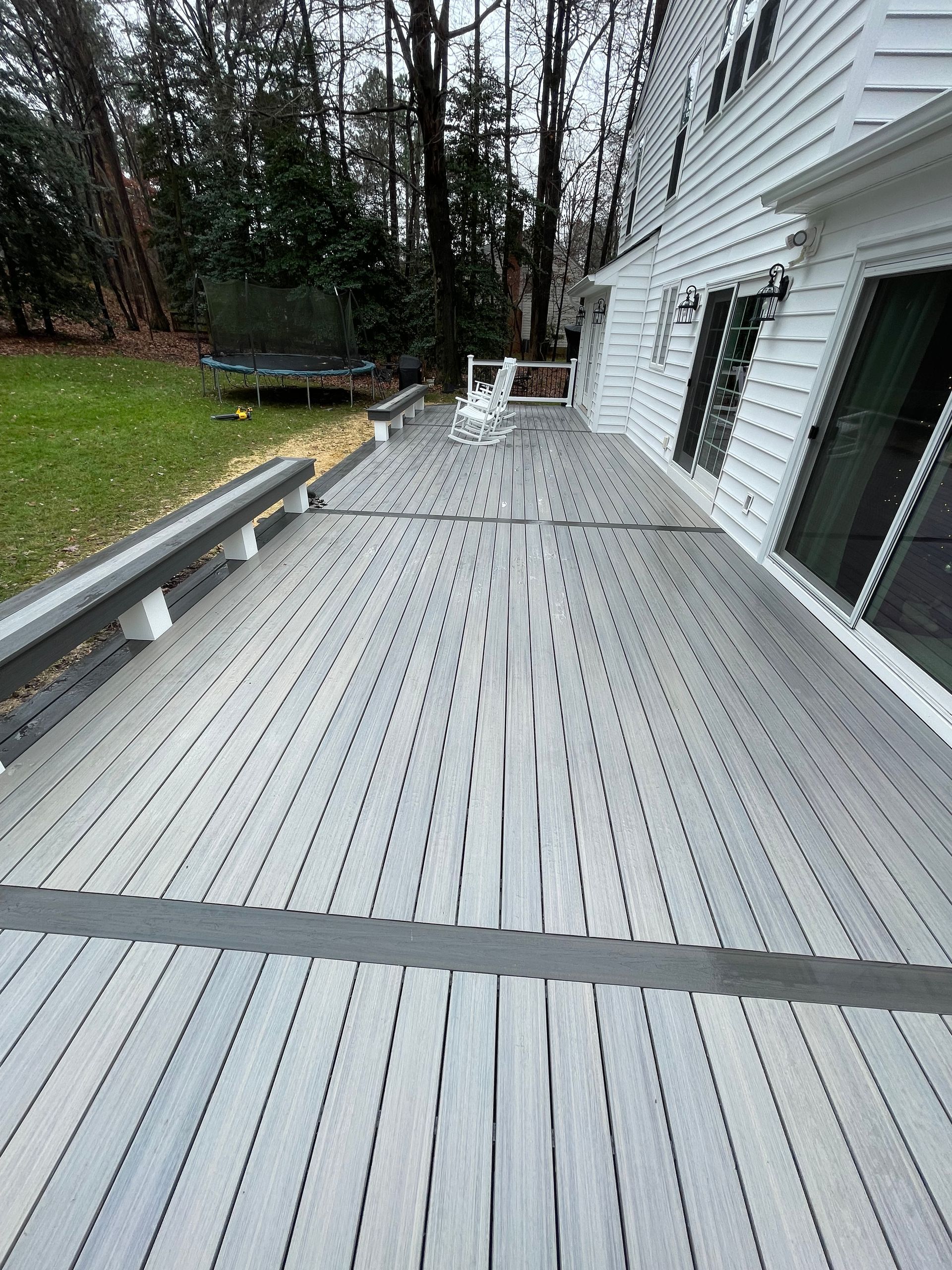 A large gray deck is sitting in front of a white house.