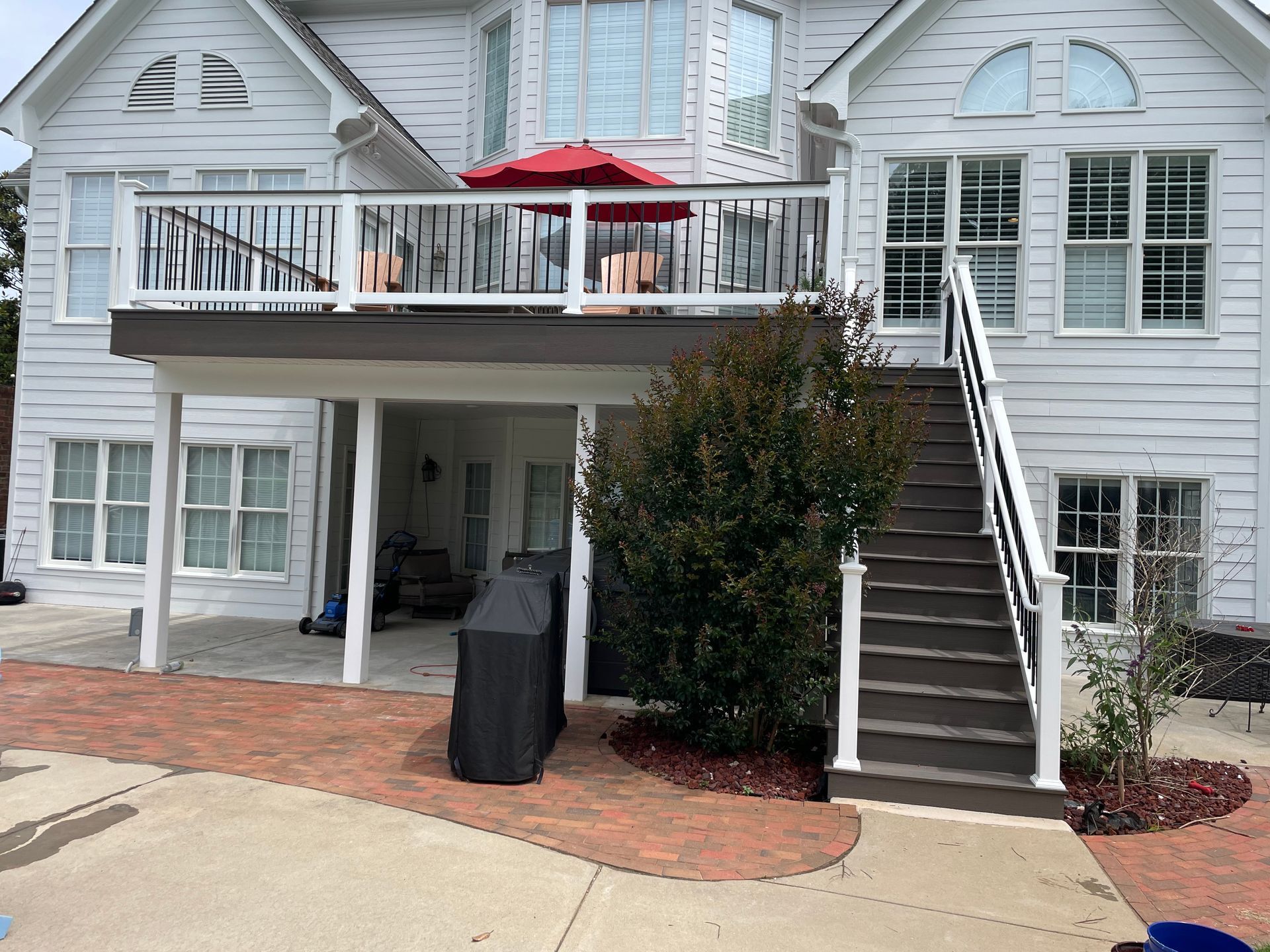 Two-story white house with a deck, stairs, and brick patio. An umbrella is on the deck.