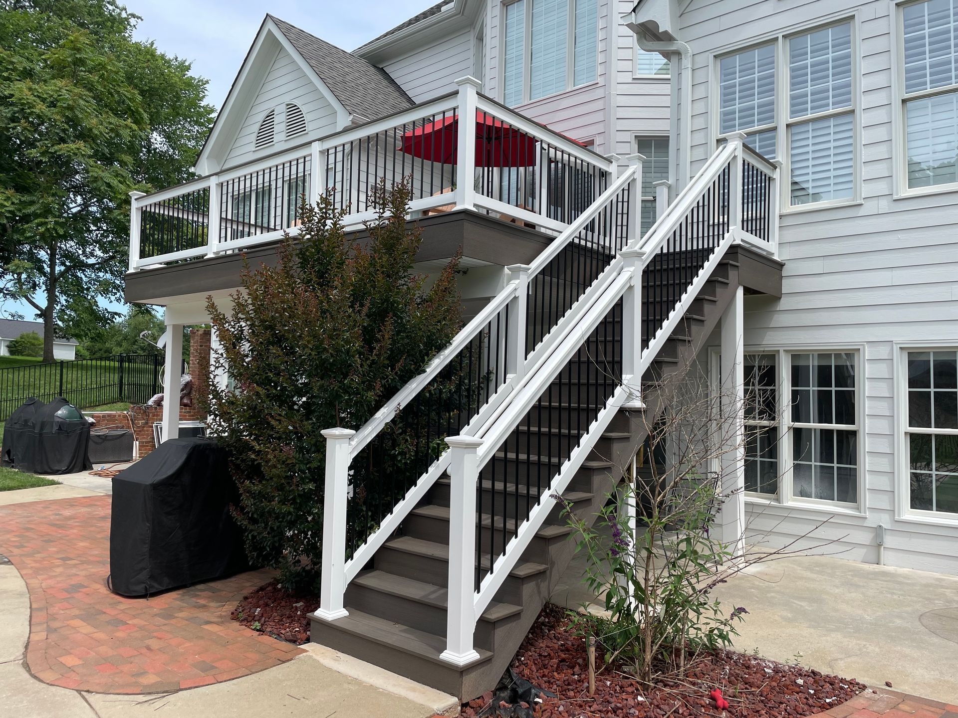 Multi-level deck with white railings, black balusters, and stairs against a white house.