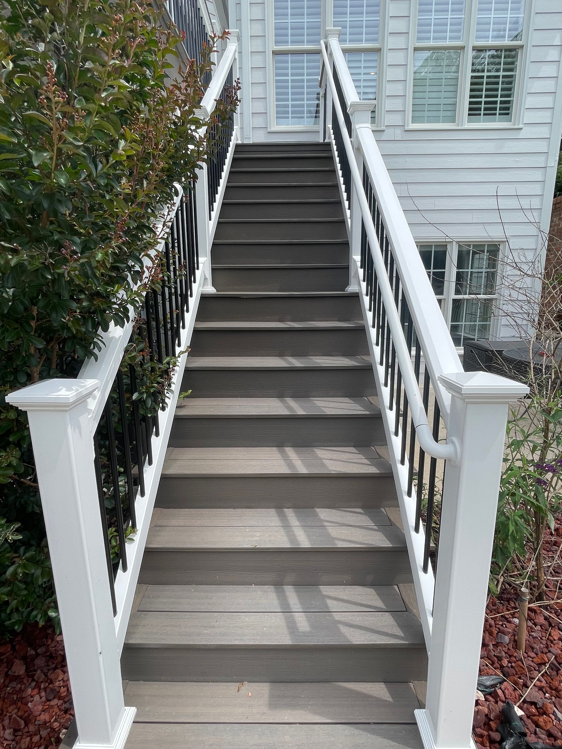 Wooden outdoor staircase with white railings, leading up to a white house with windows.