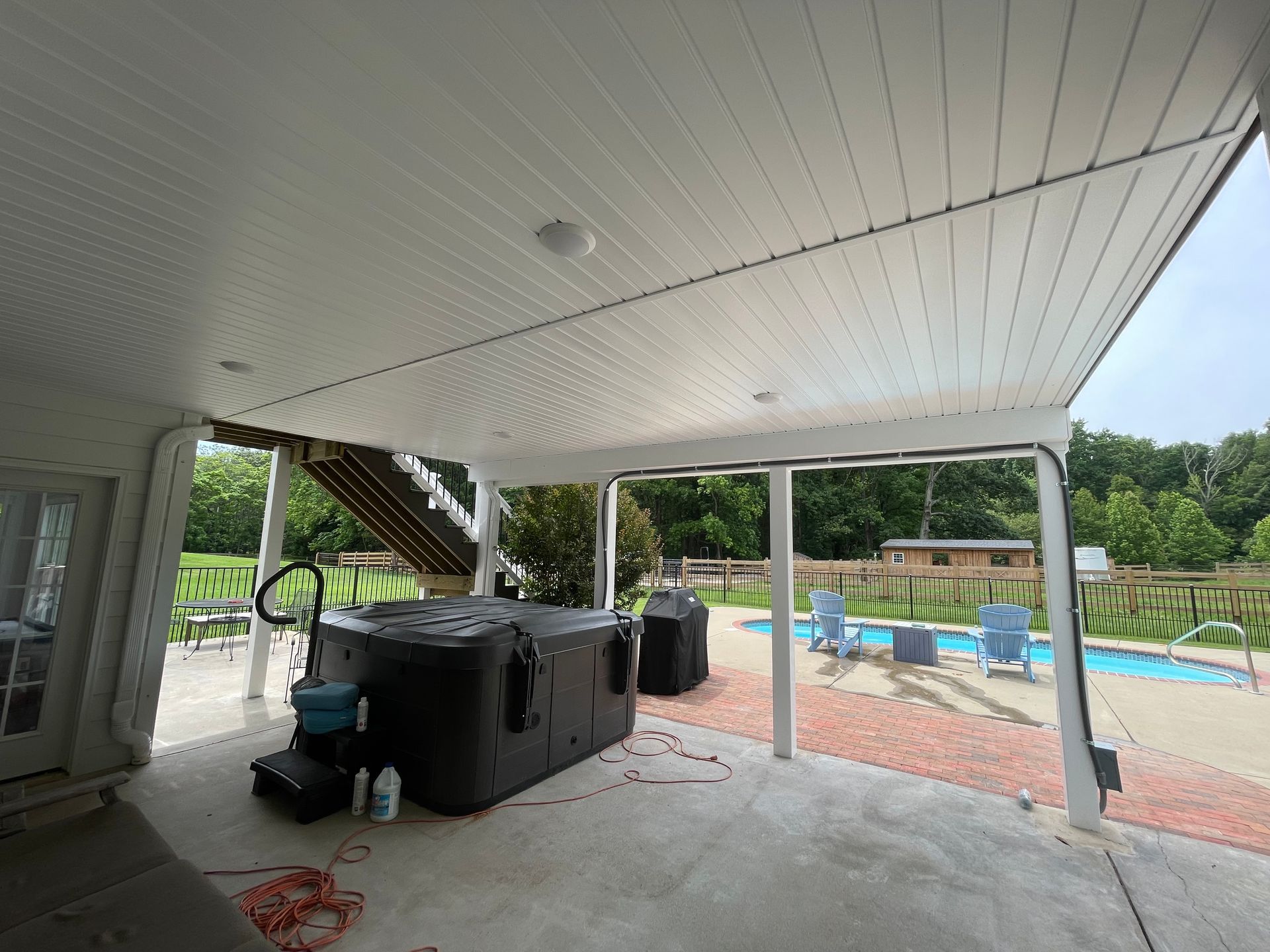 Covered patio with a hot tub, pool, and trees in the background.