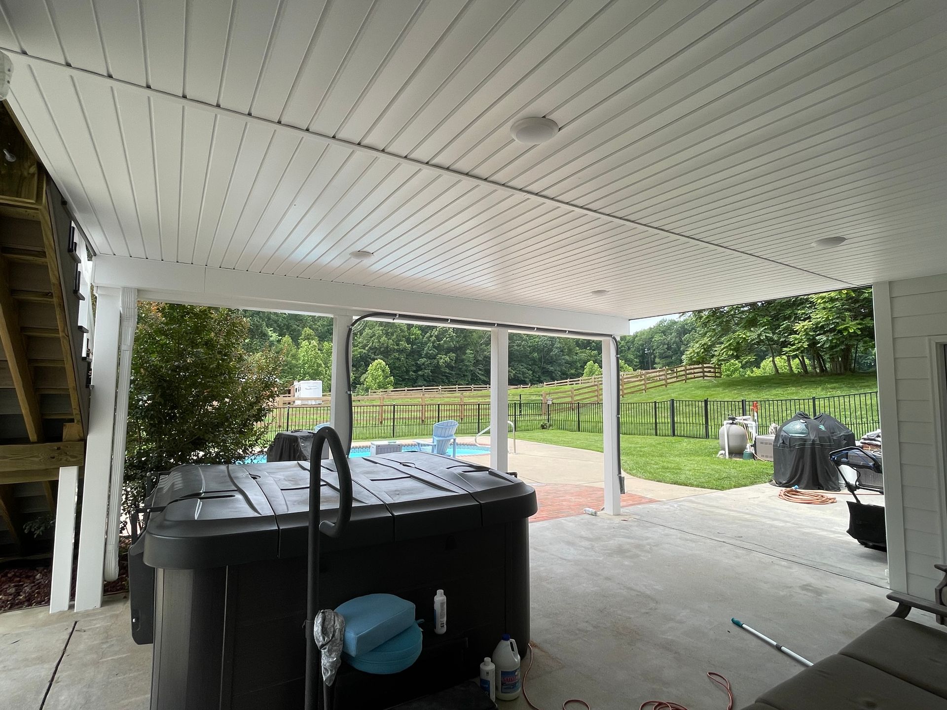 Patio with hot tub under a white ceiling, overlooking a pool and yard.