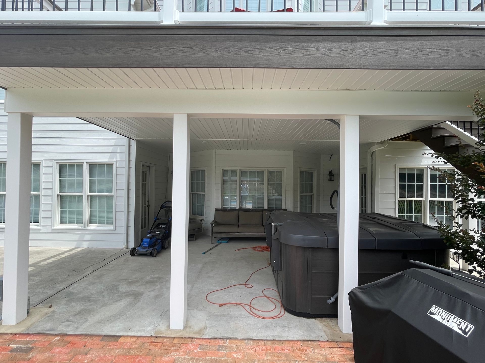 Covered patio with white columns and ceiling, concrete floor, hot tubs, and house exterior.