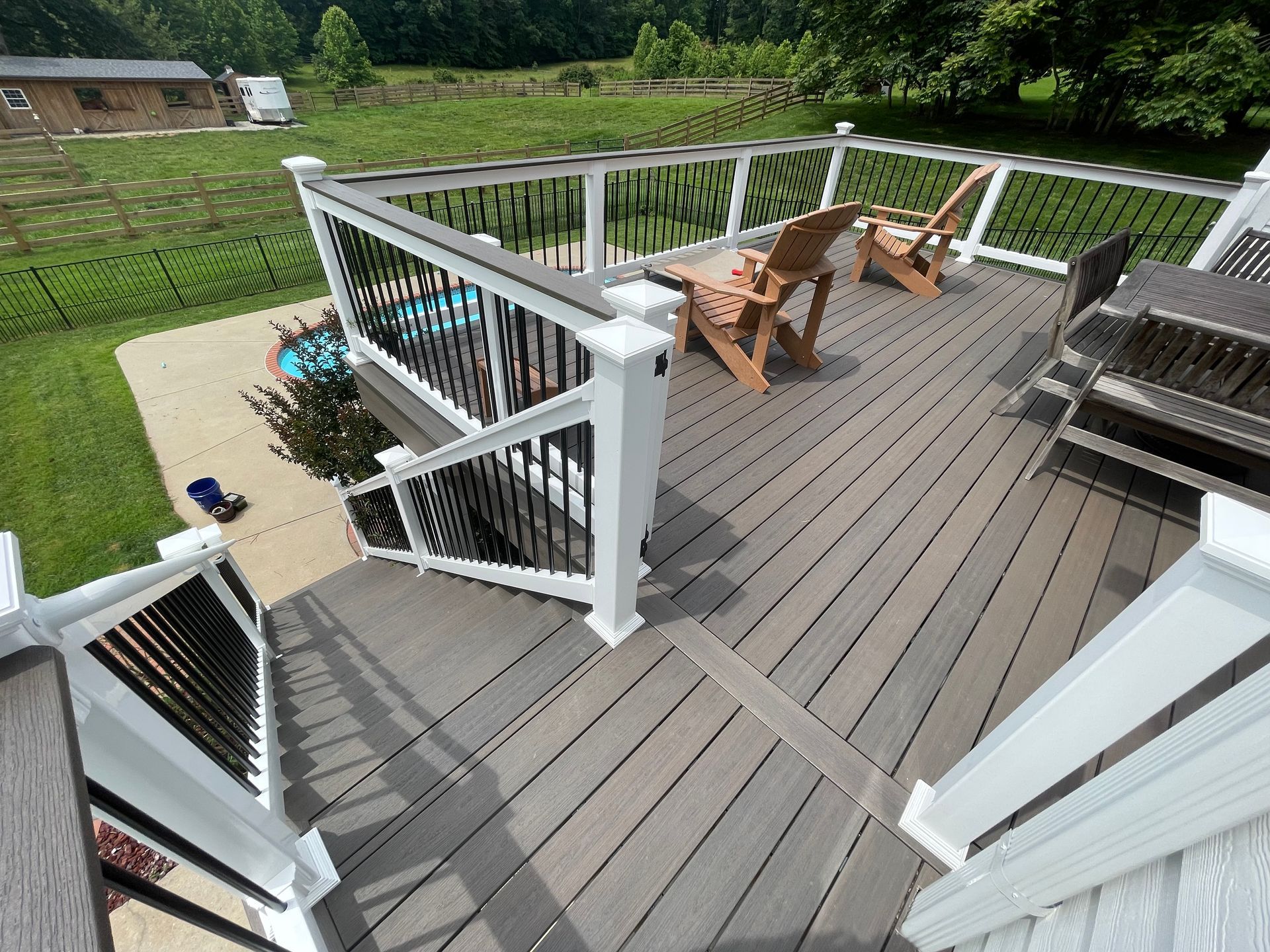 Composite deck with black railing and white posts, two chairs, overlooking a pool.