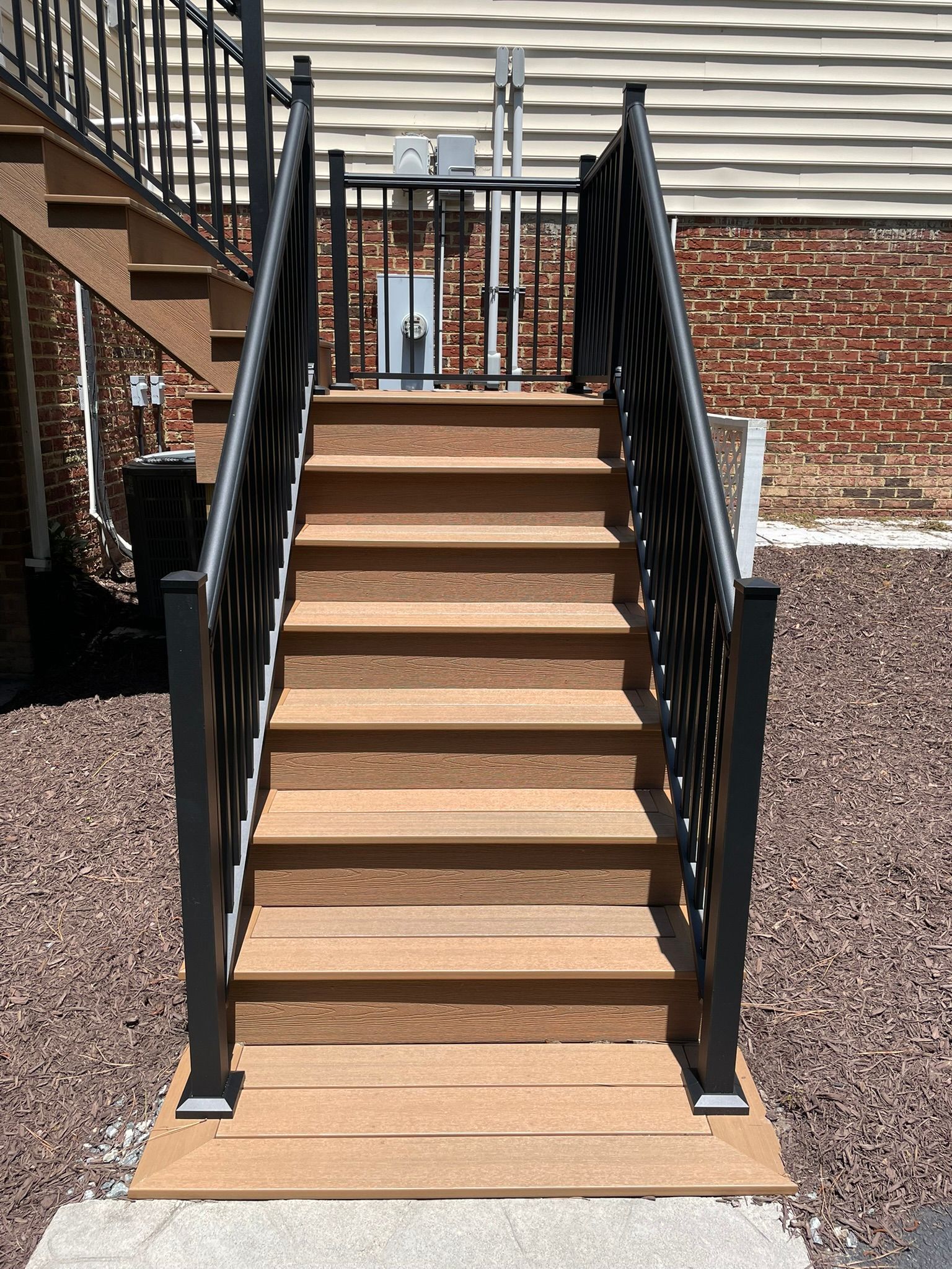 Wooden outdoor staircase with black railing, leading up to a platform.