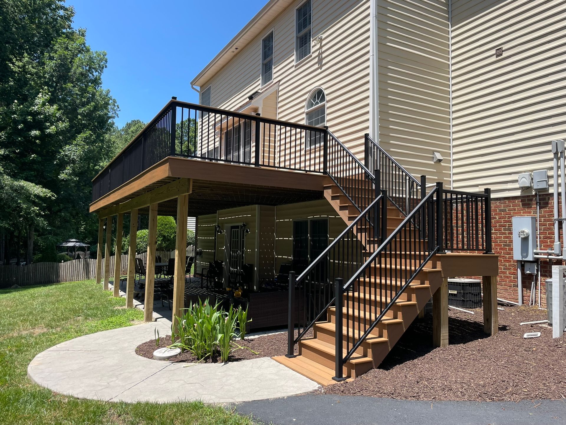 Two-story deck with black railings and brown steps, next to a tan house.
