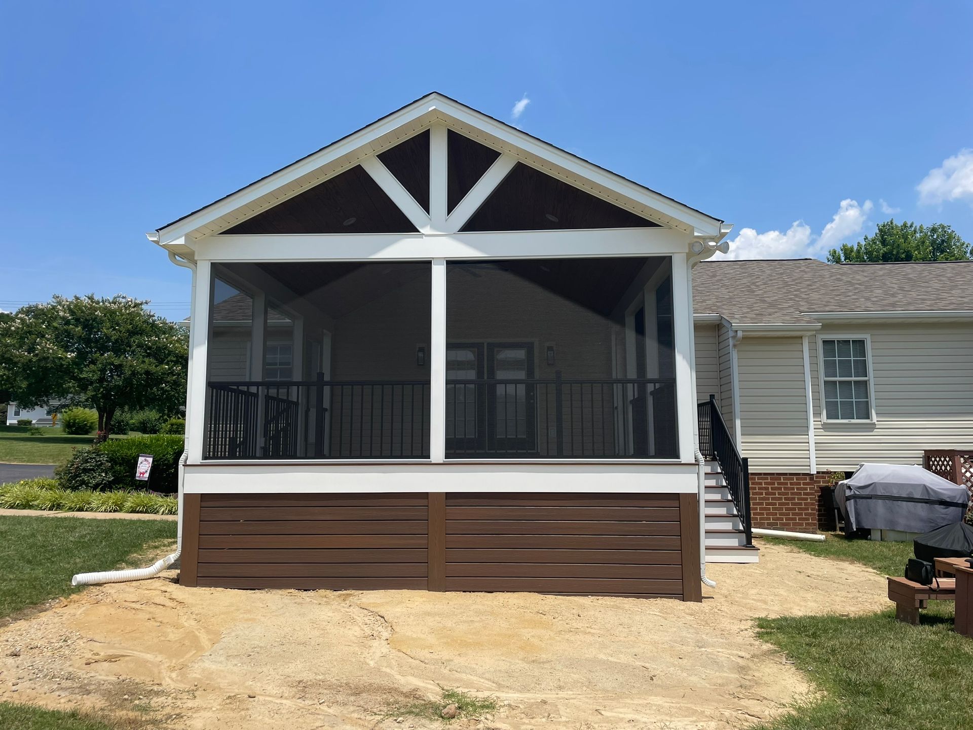 Screened porch with brown siding, white trim, and a gabled roof. Exterior of a house.