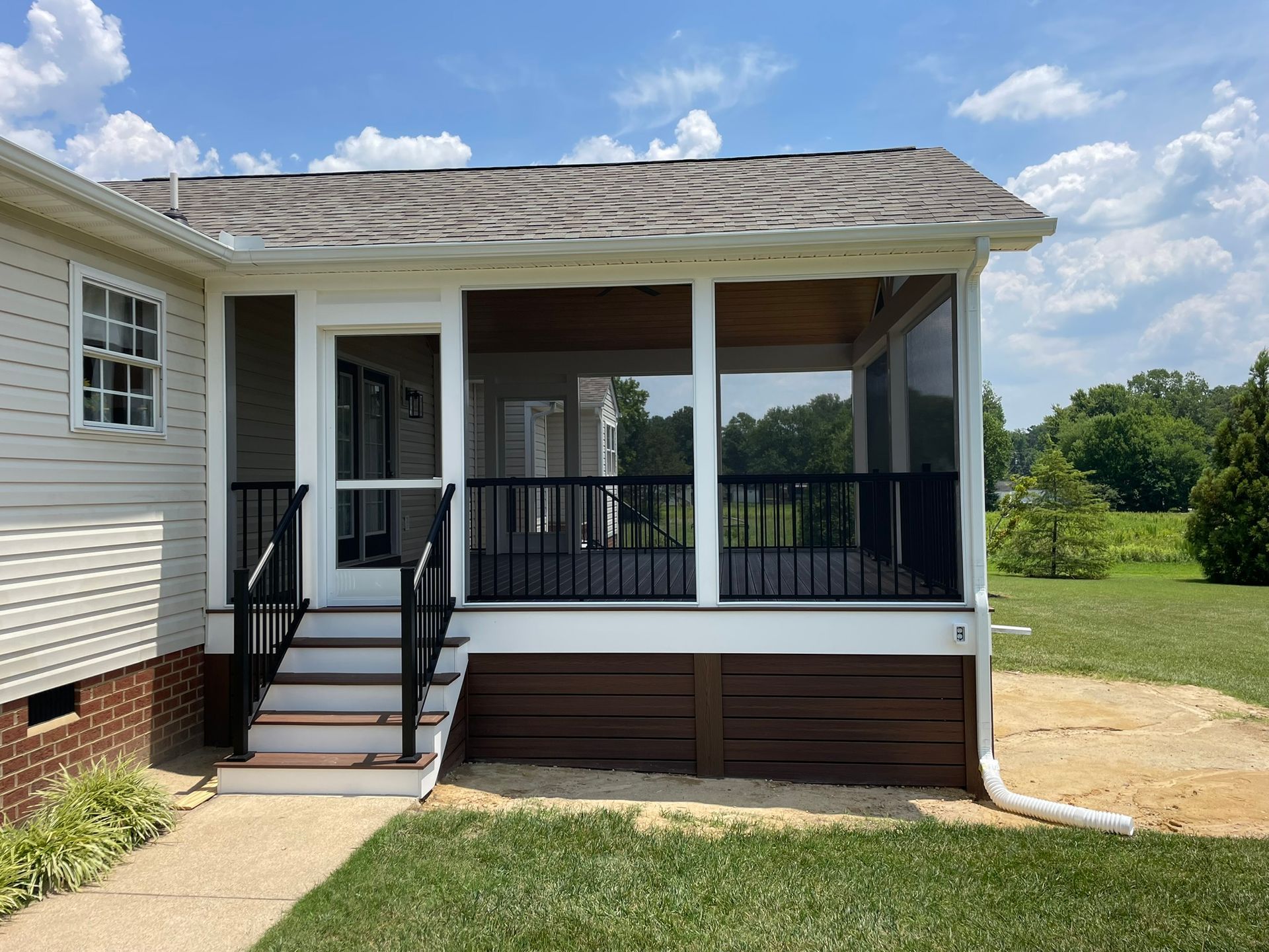 Screened porch with black railings, brown siding, and white trim, next to a beige house, with a grassy yard.