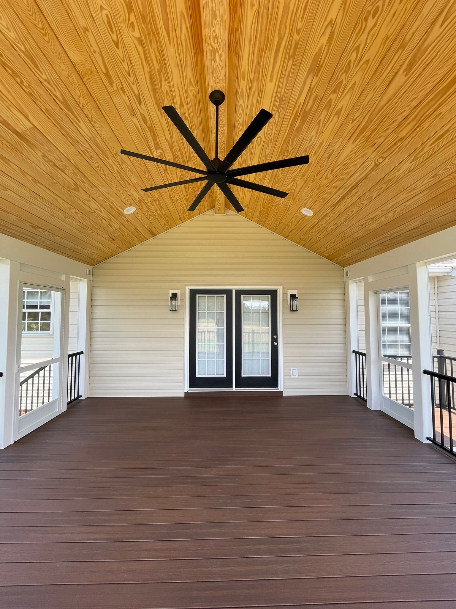 Covered porch with wood ceiling, dark composite decking, black ceiling fan, and double doors.