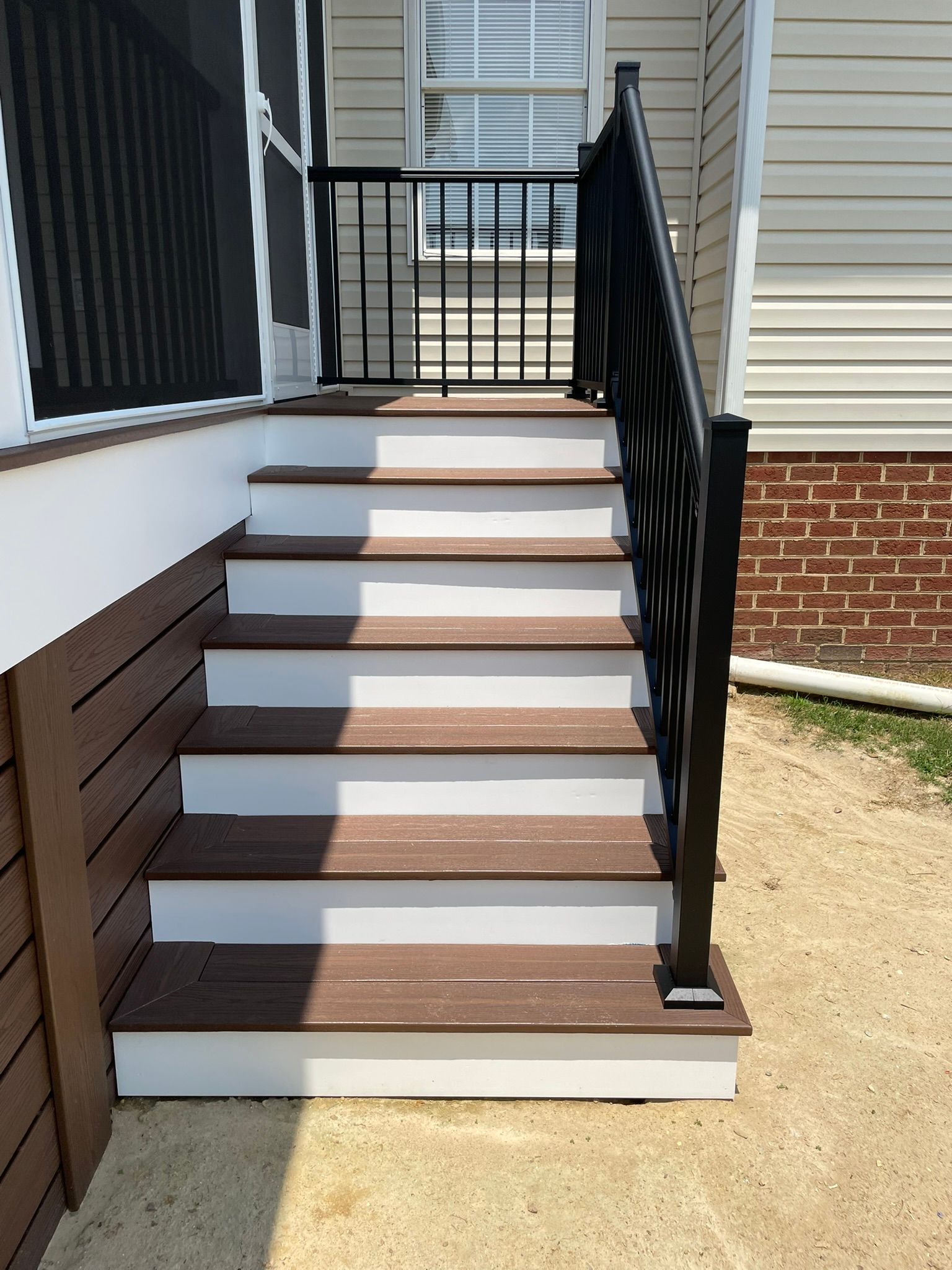 Brown and white outdoor staircase with black railing leading to a doorway, set against beige siding.