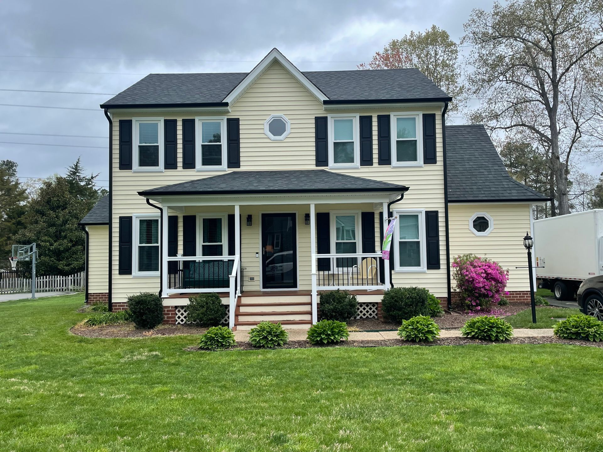 A large yellow house with black shutters is sitting on top of a lush green lawn.