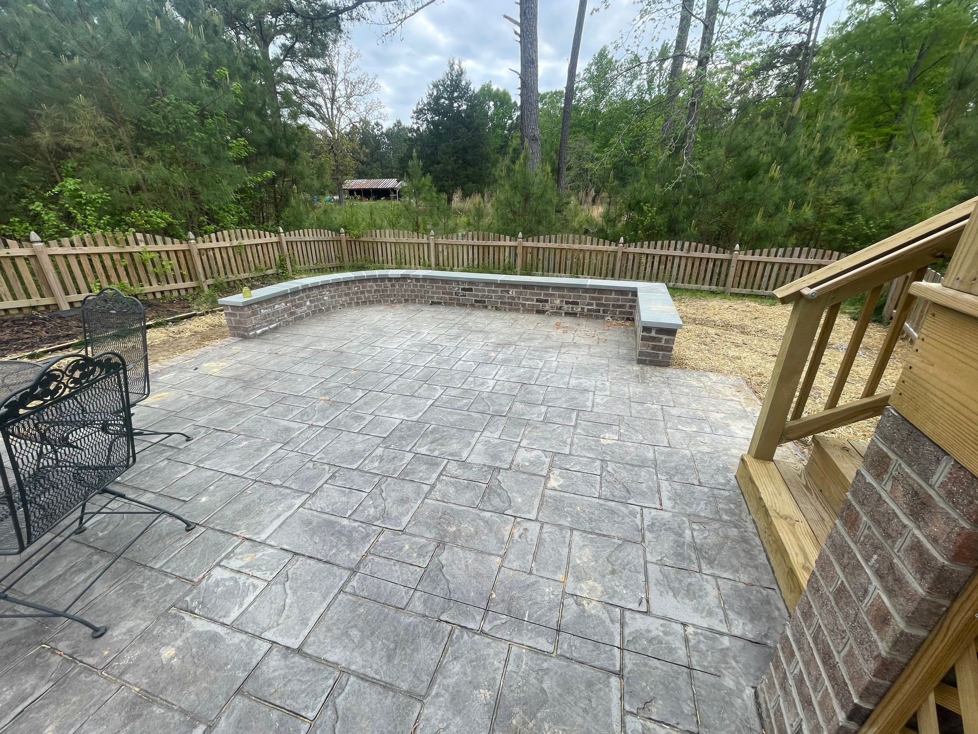 A patio with a bench and chairs and a fence in the background.