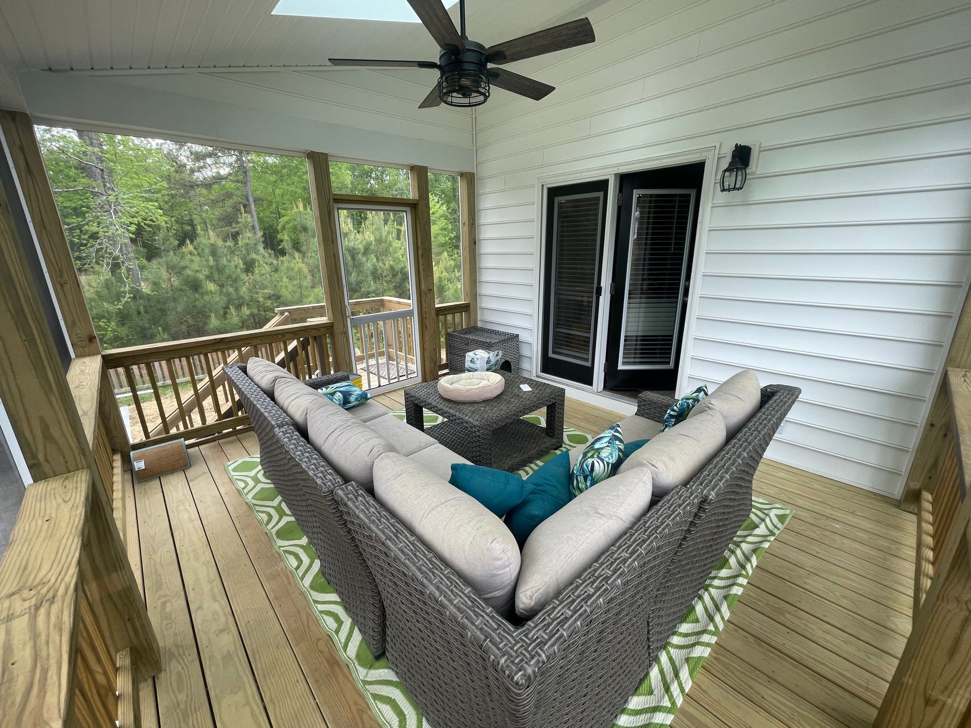 A screened in porch with a couch , table , and ceiling fan.