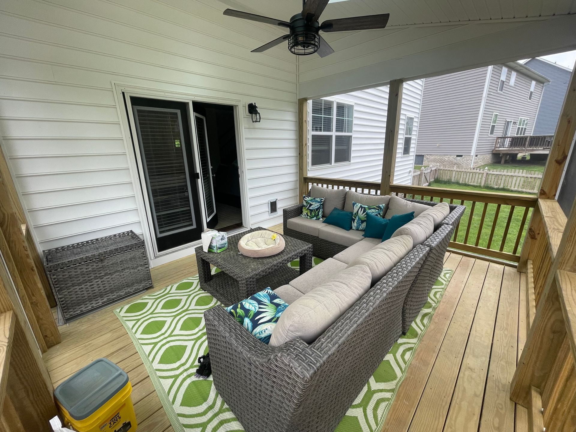 A screened in porch with a sectional couch and a ceiling fan.