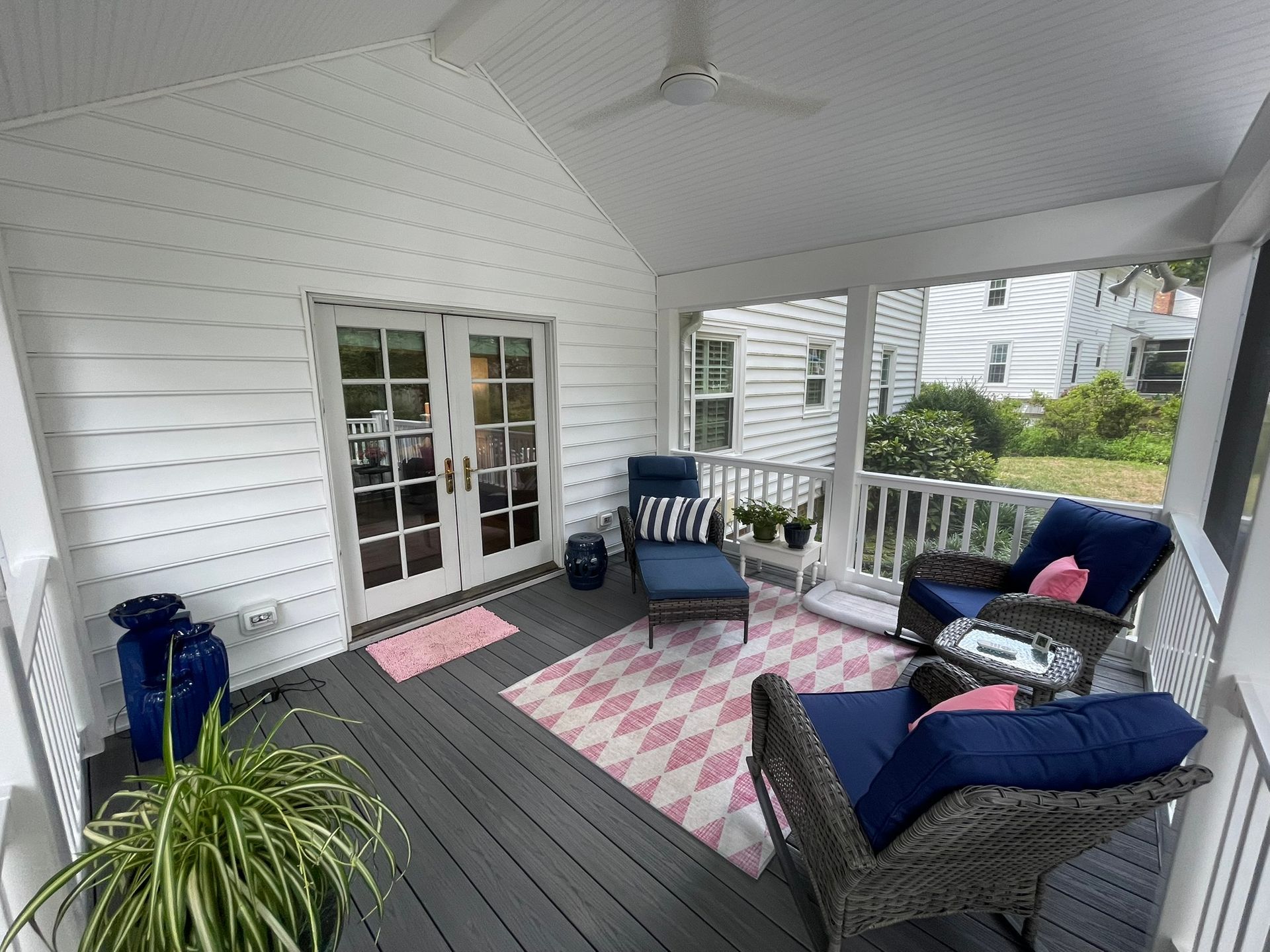 Enclosed porch with gray floor and white walls. Blue wicker furniture with pink and blue accents.