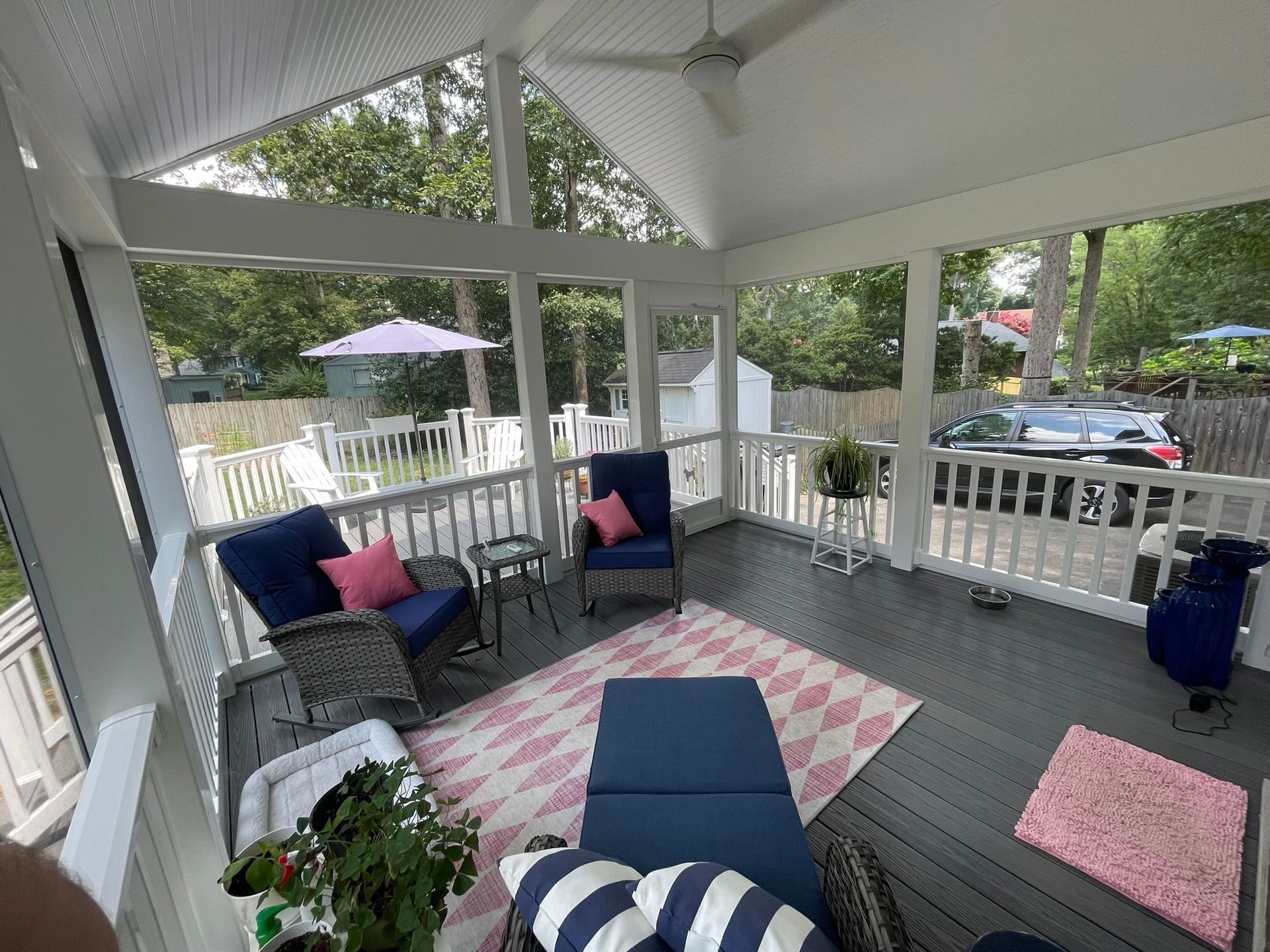Screened porch with blue furniture, pink rug, and view of a yard.