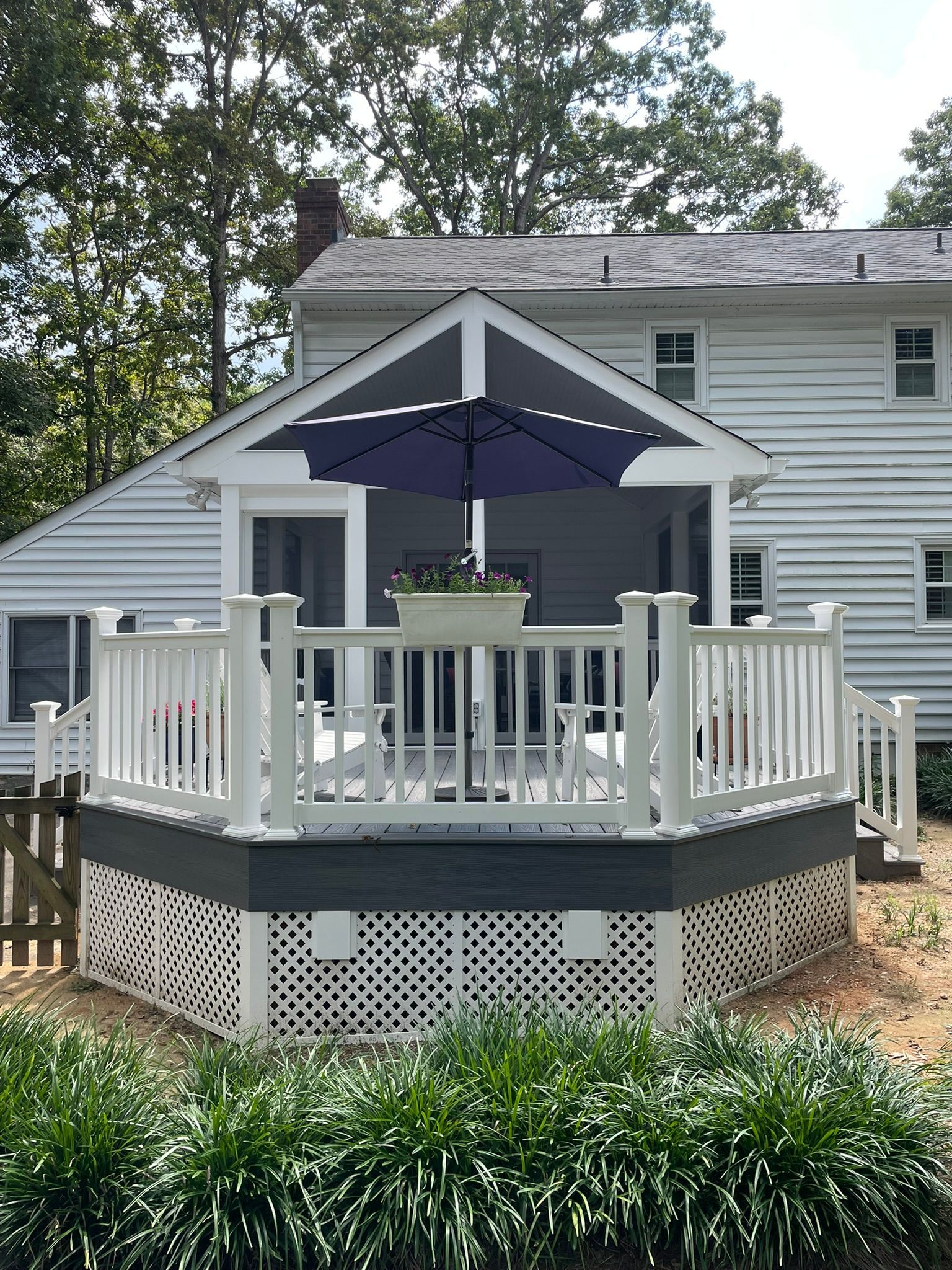 White deck with a screened porch, blue umbrella, and flowering plants.