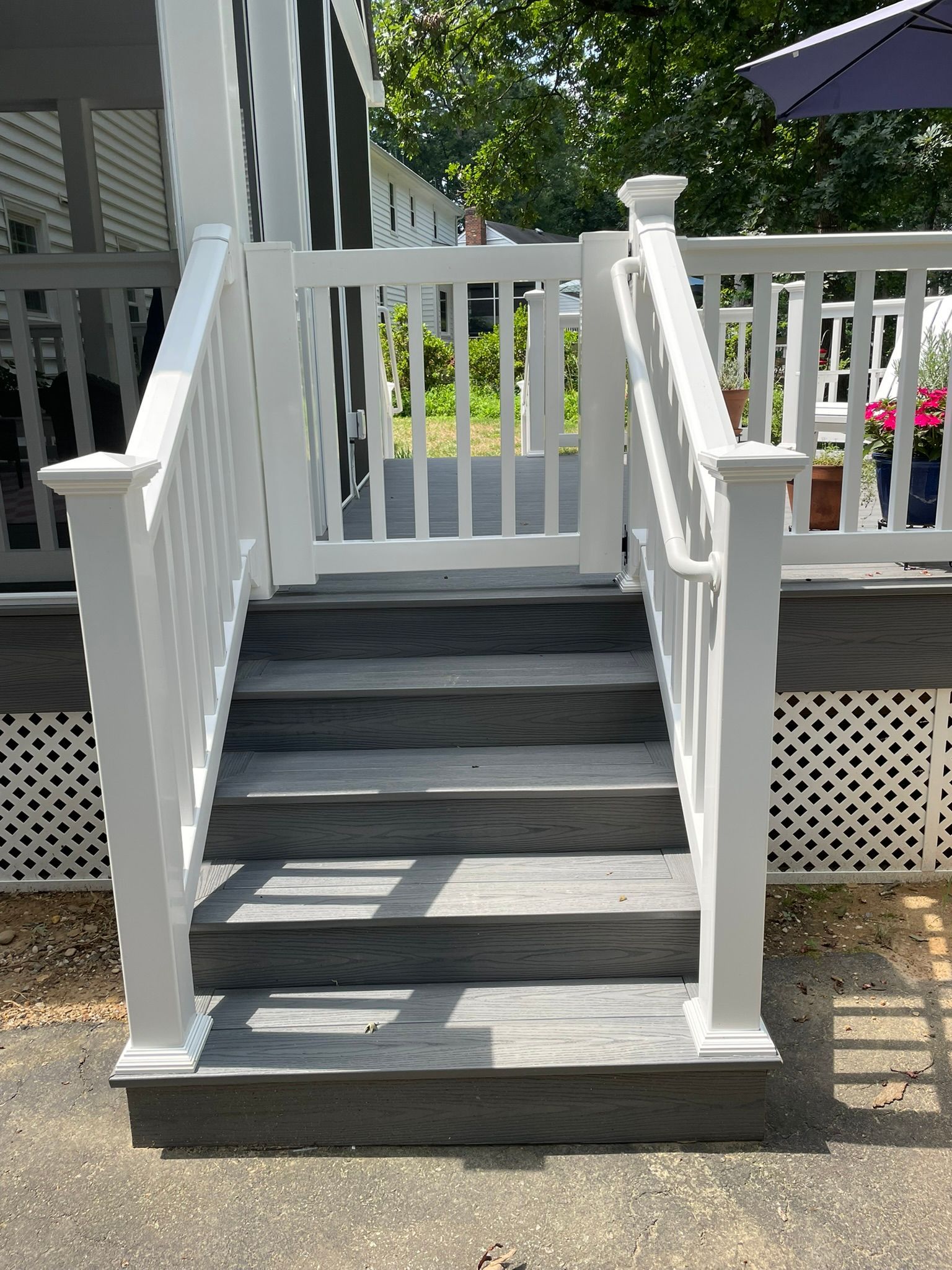 White-railed staircase leading to a gate on an outdoor deck. Gray steps, white railings. Sunny day.