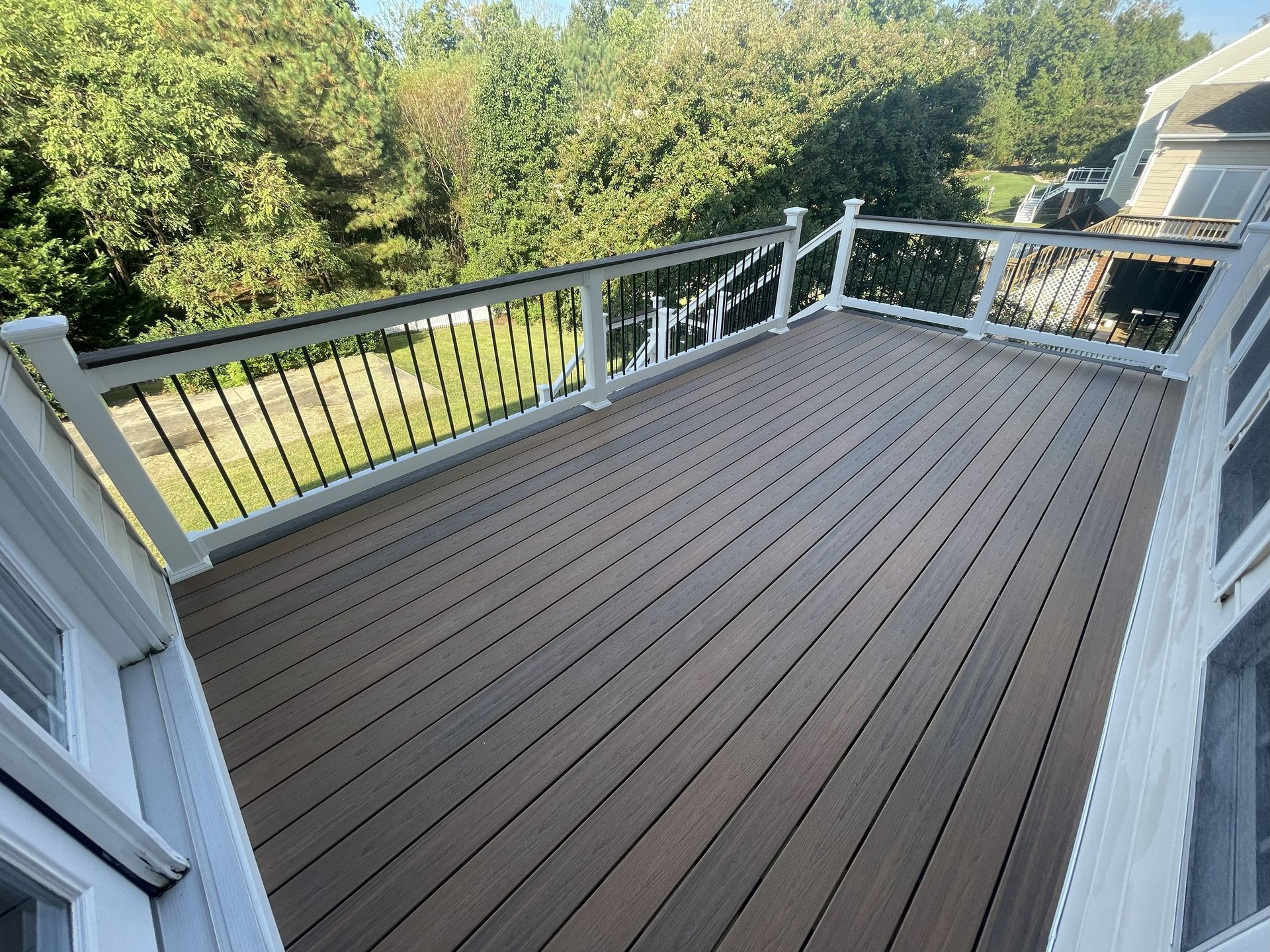 Brown composite deck with white railing and black spindles, overlooking trees.