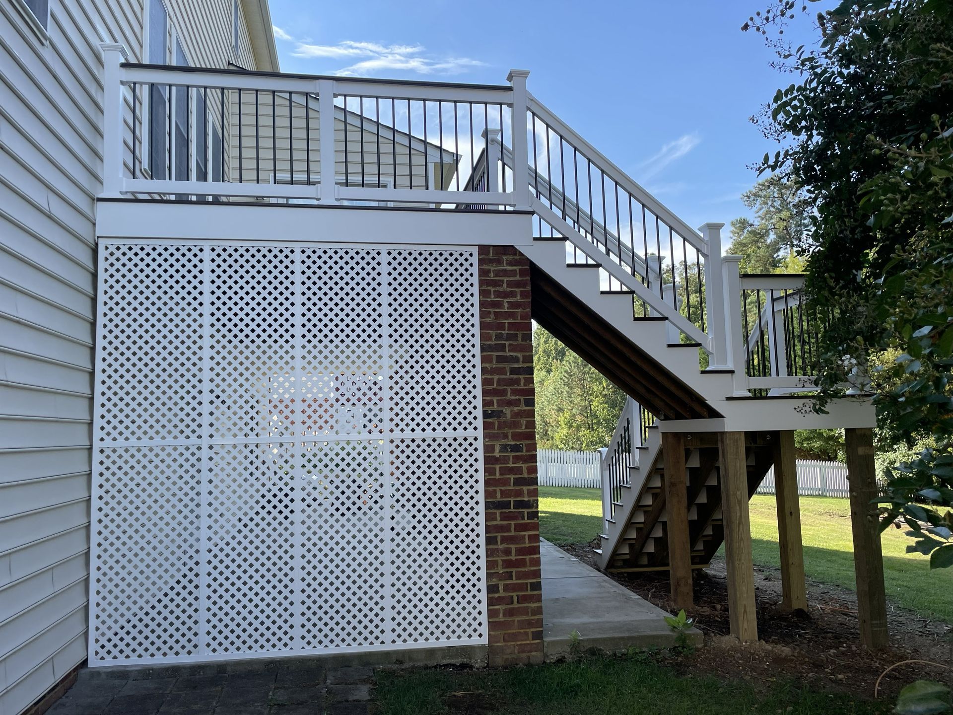 White deck with lattice skirting, brick support, and stairs. Blue sky and green grass in the background.