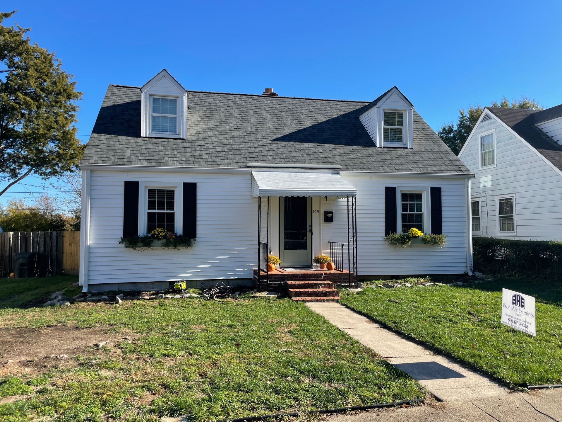 A white house with black shutters and a sign in front of it.