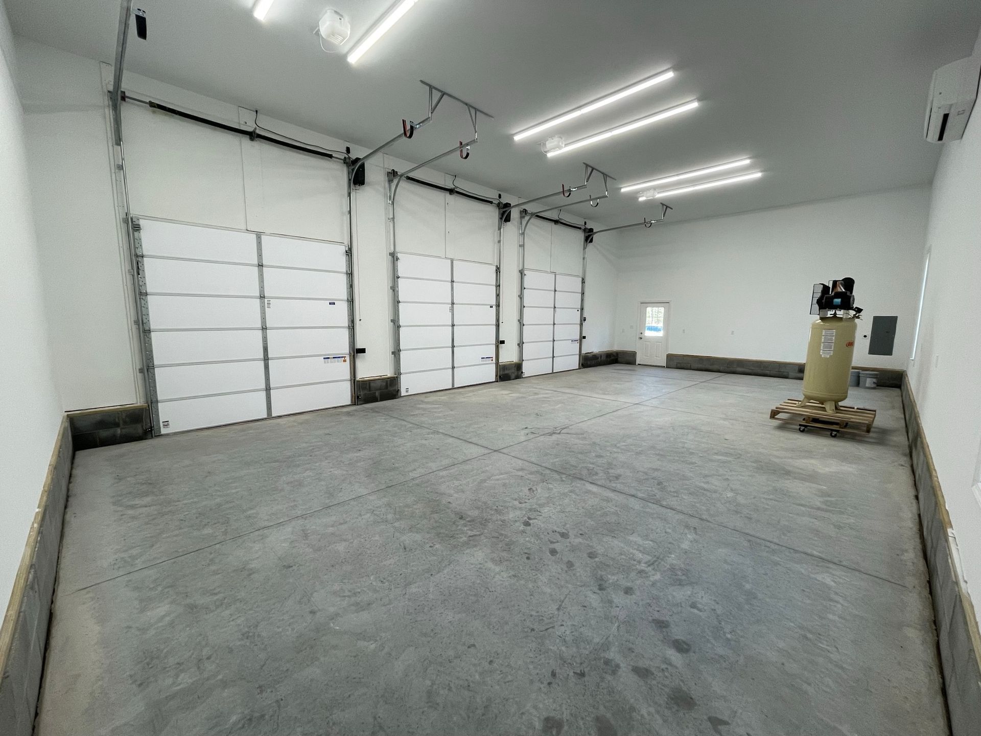 Empty garage with three overhead doors, gray concrete floor, white walls, and bright overhead lights.