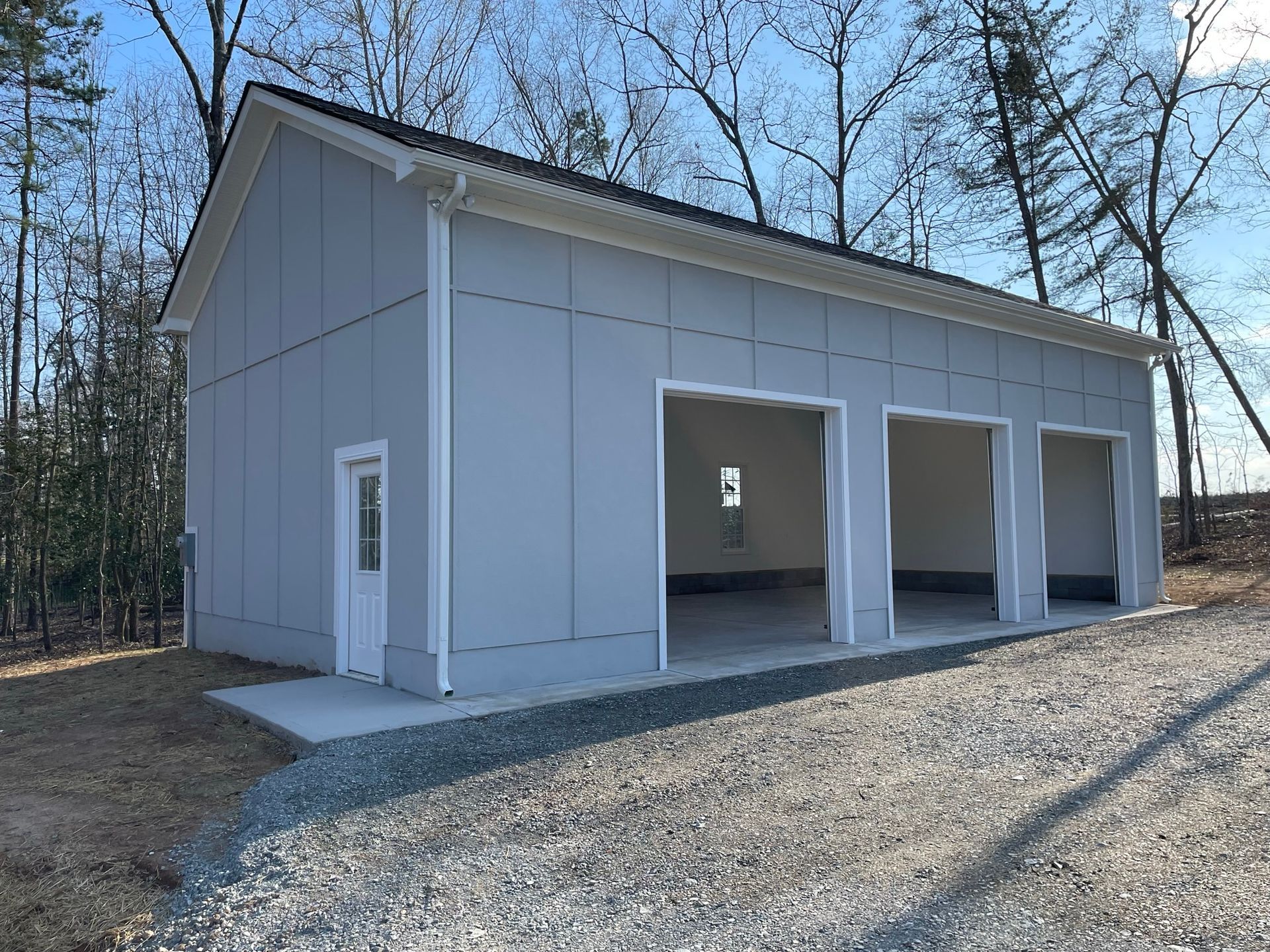 Light blue three-bay garage with white trim and door. Gravel driveway.