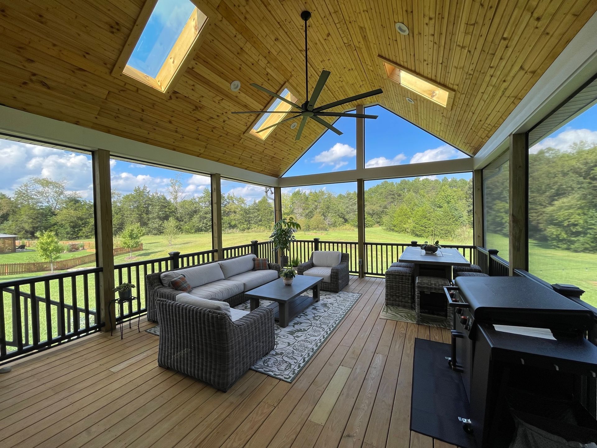 A screened in porch with a lot of furniture and a ceiling fan.