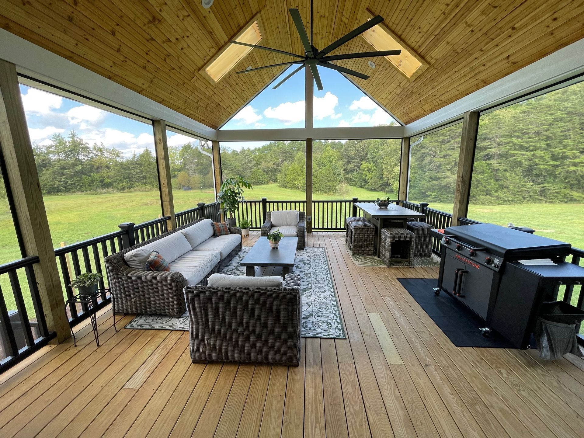 A screened in porch with a lot of furniture and a ceiling fan.