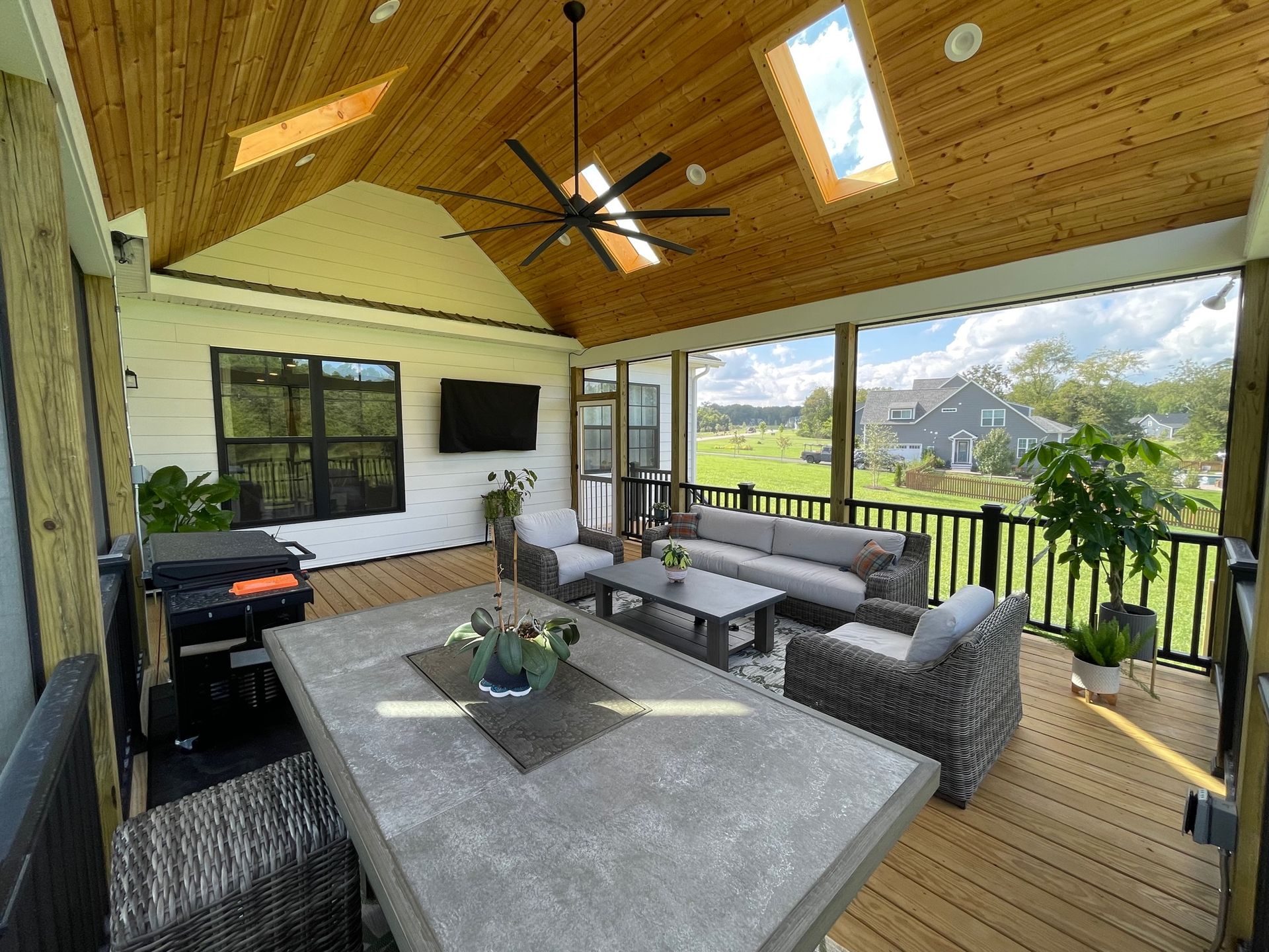 A screened in porch with a table and chairs and a ceiling fan.