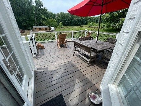 View from a doorway onto a backyard deck with outdoor dining set, chairs, and a red umbrella.