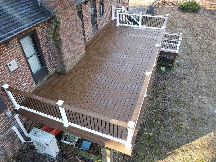 A large elevated brown deck with white railings attached to a brick house overlooking the yard below A large elevated brown deck with white railings attached to a brick house overlooking the yard below