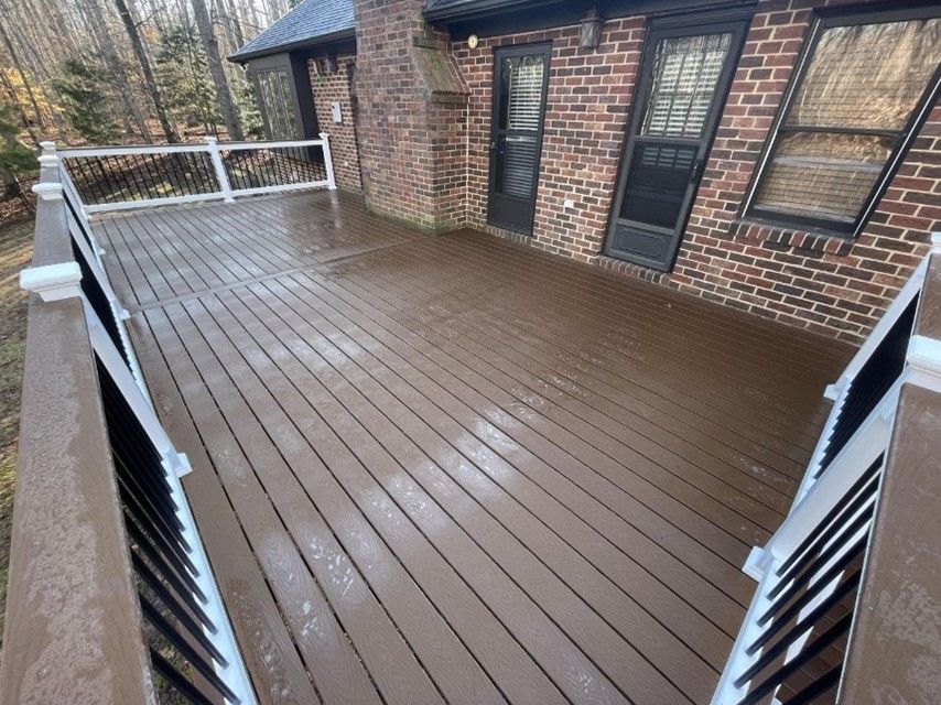 A spacious wooden deck with black and white railings attached to a brick house with trees A spacious wooden deck with black and white railings attached to a brick house with trees