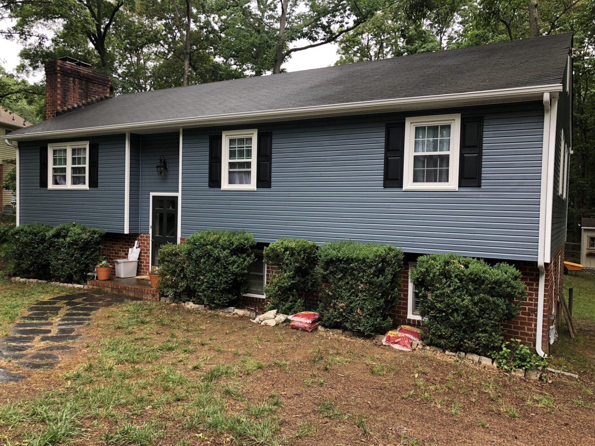 A blue house with black shutters is sitting on top of a lush green field.