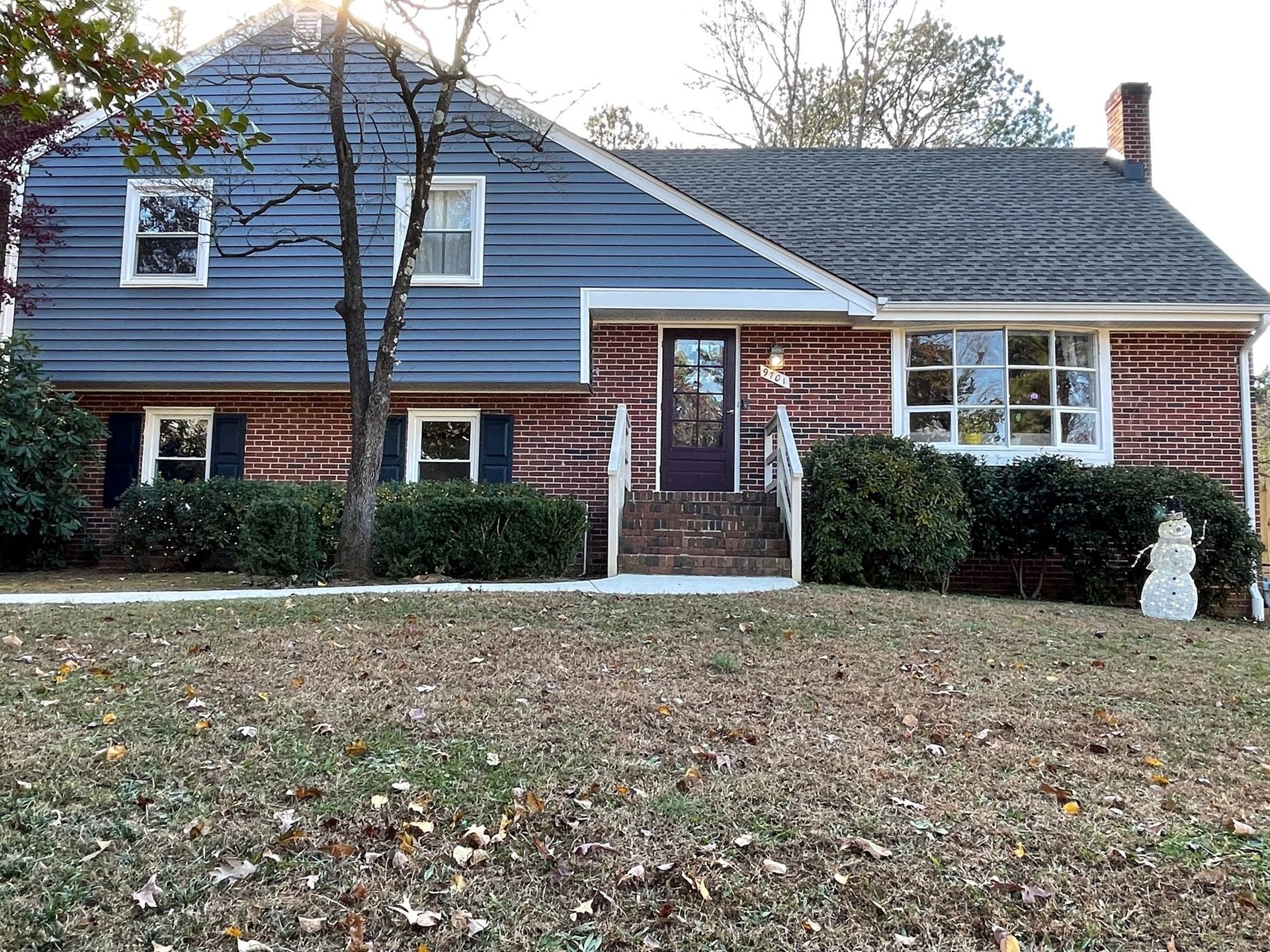 A large house with a blue siding and a snowman in front of it.