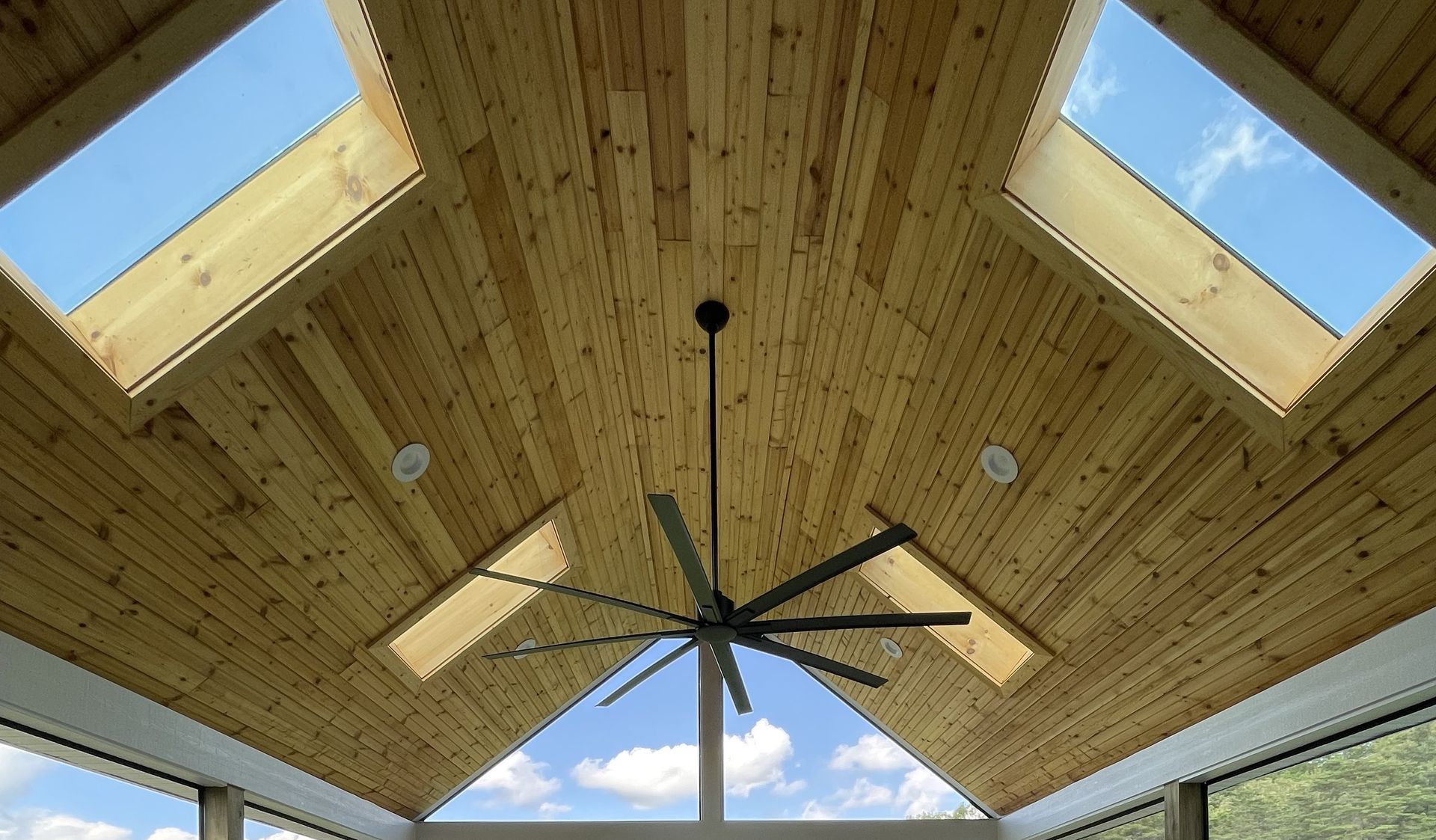 A ceiling fan is hanging from the ceiling of a room with a wooden ceiling and skylights.