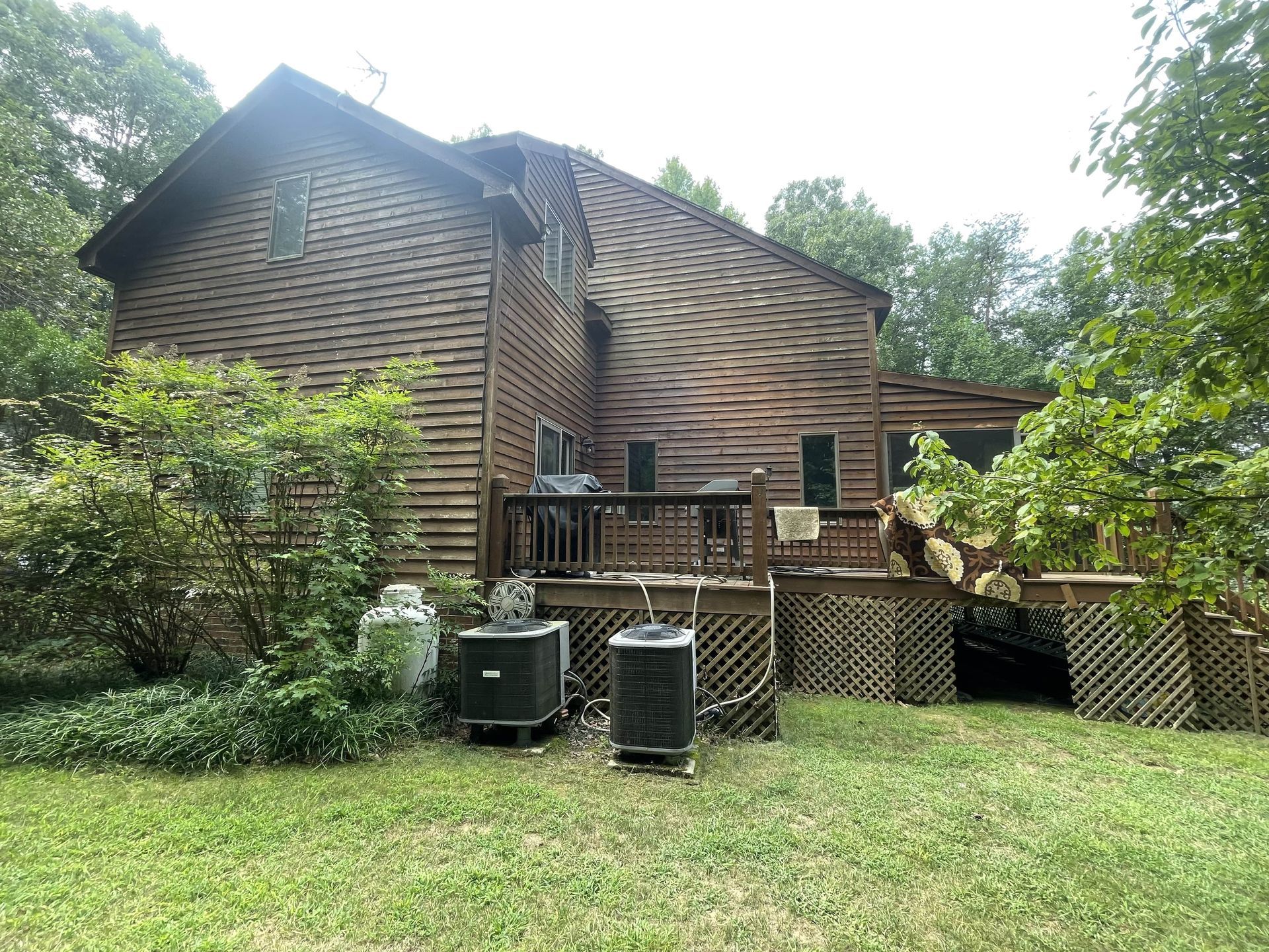 A large wooden house with a deck and air conditioners in the backyard.