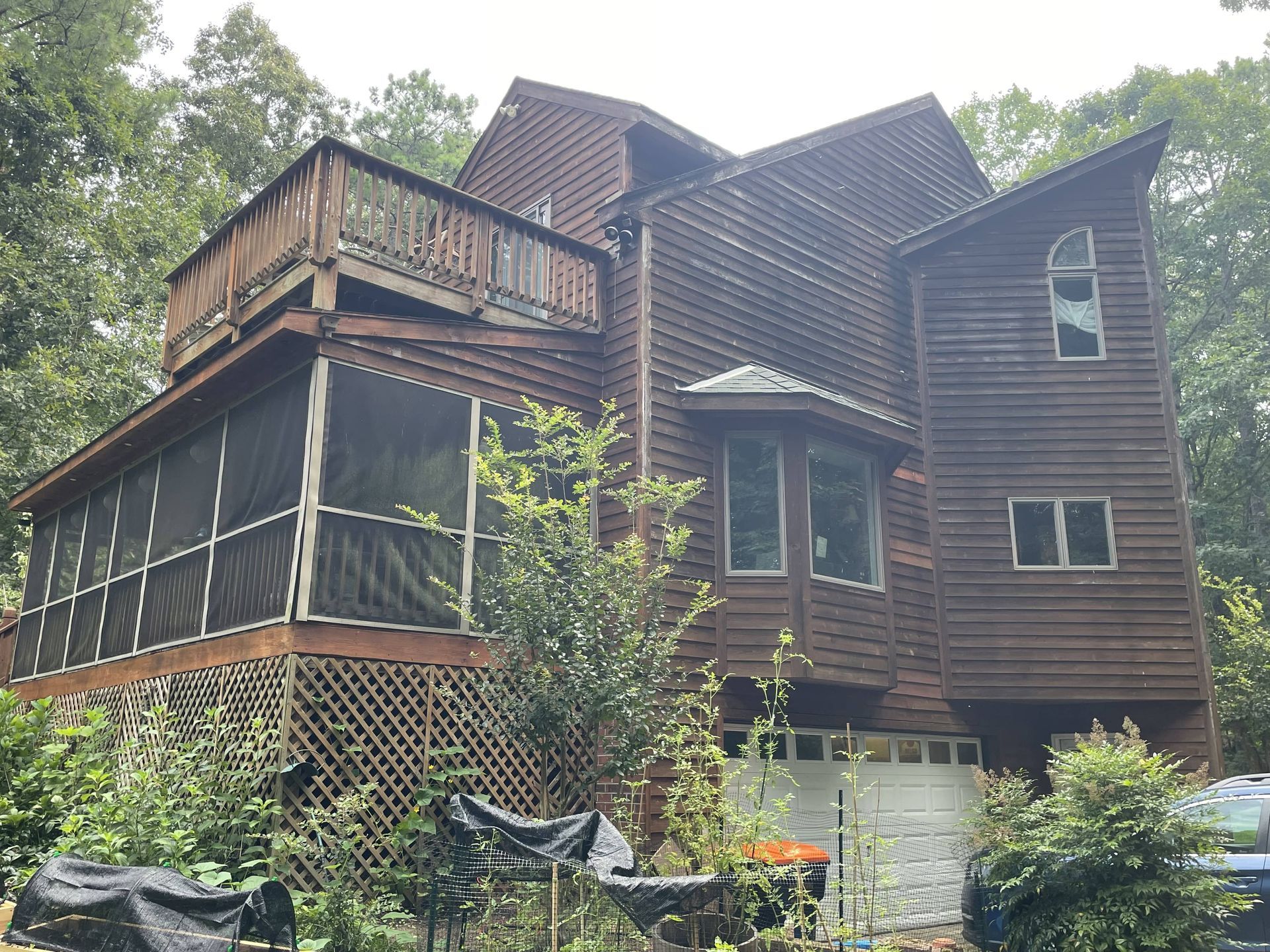 A large wooden house with a screened in porch and a car parked in front of it
